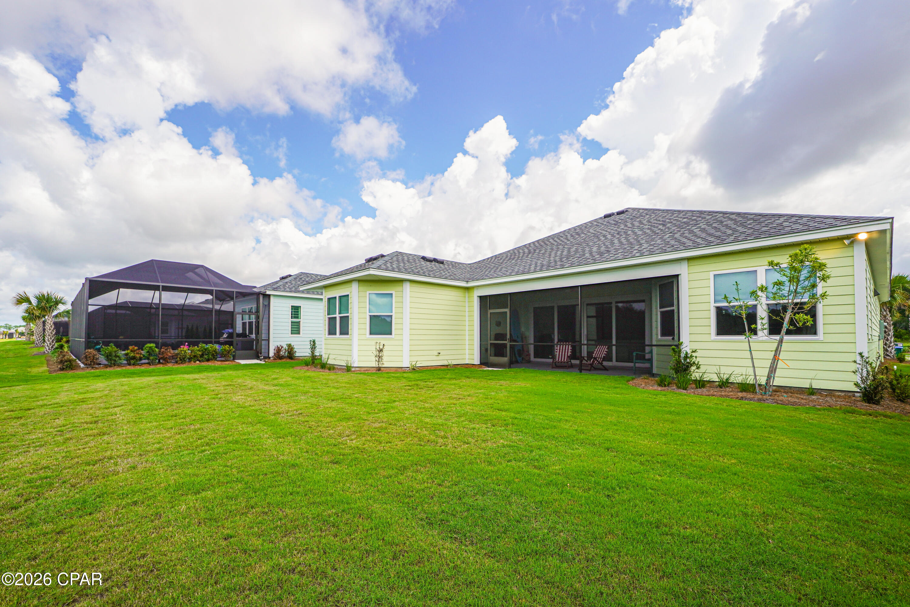 Rear of a light-yellow home with a screened porch and wide green lawn.