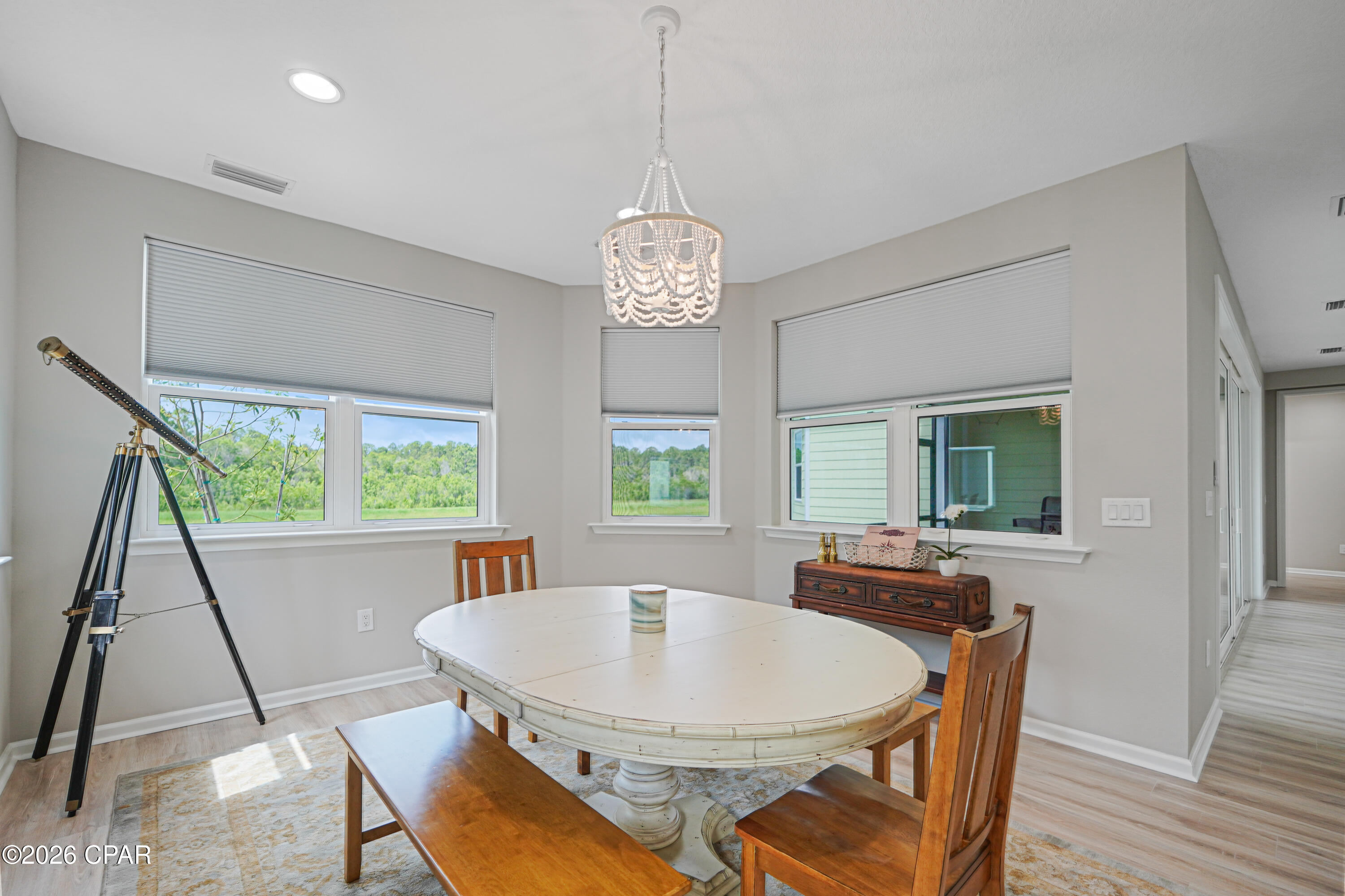 Dining room with an oval table, beaded chandelier, telescope, and large windows overlooking greenery.