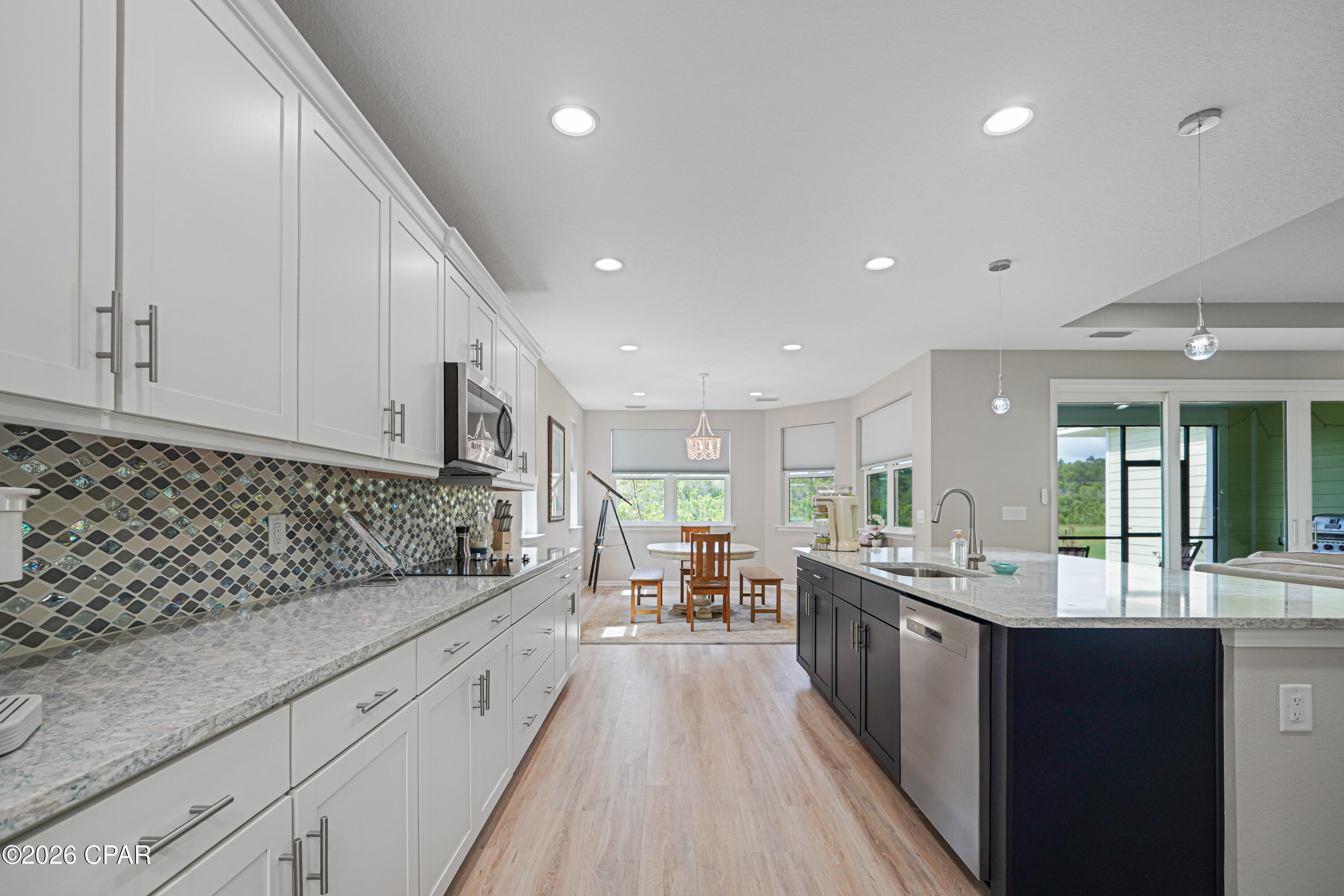 Open-plan kitchen with white cabinets, patterned tile backsplash, and a dark island beside the dining area.