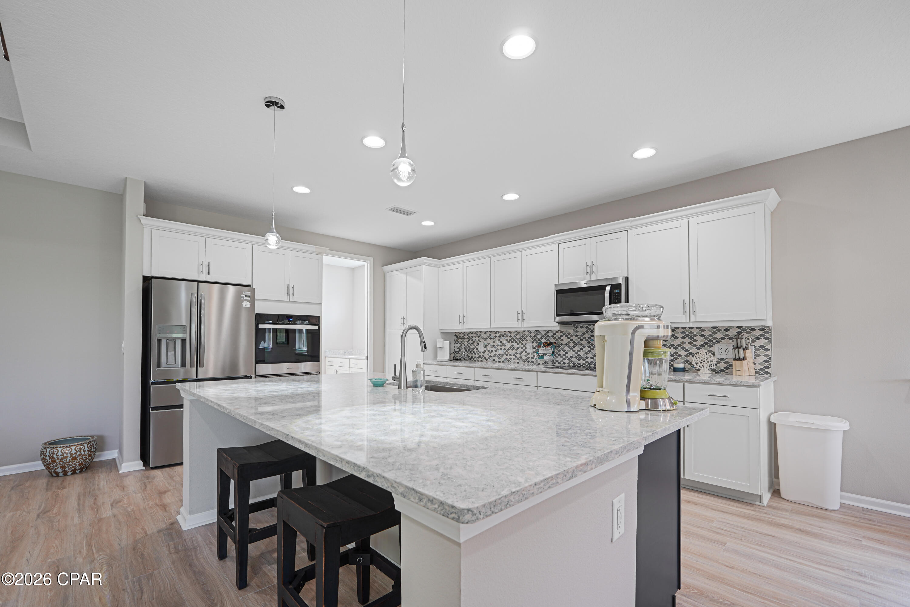 Kitchen with white cabinetry, stainless steel appliances, patterned backsplash, and a large stone island.