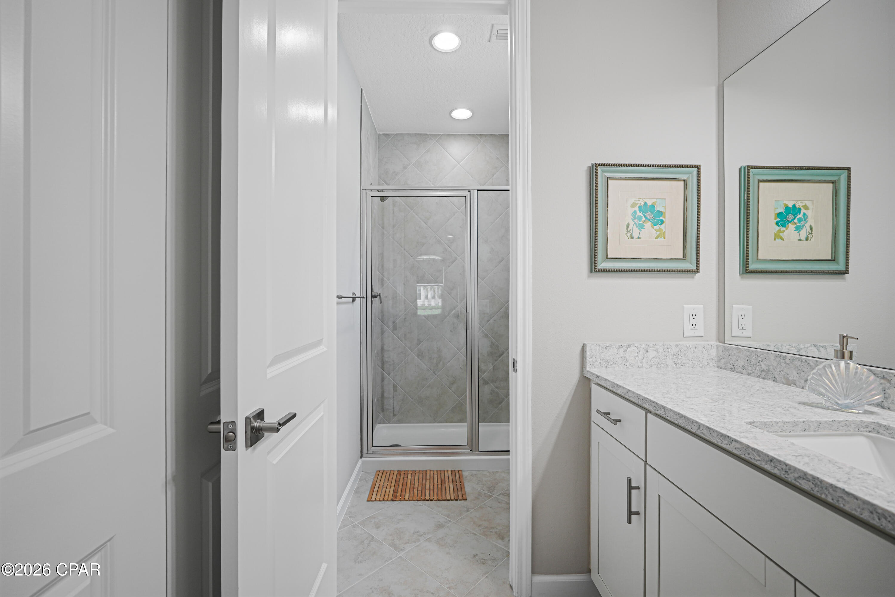 Bathroom with a glass shower, gray tile, and a white vanity with a stone countertop.