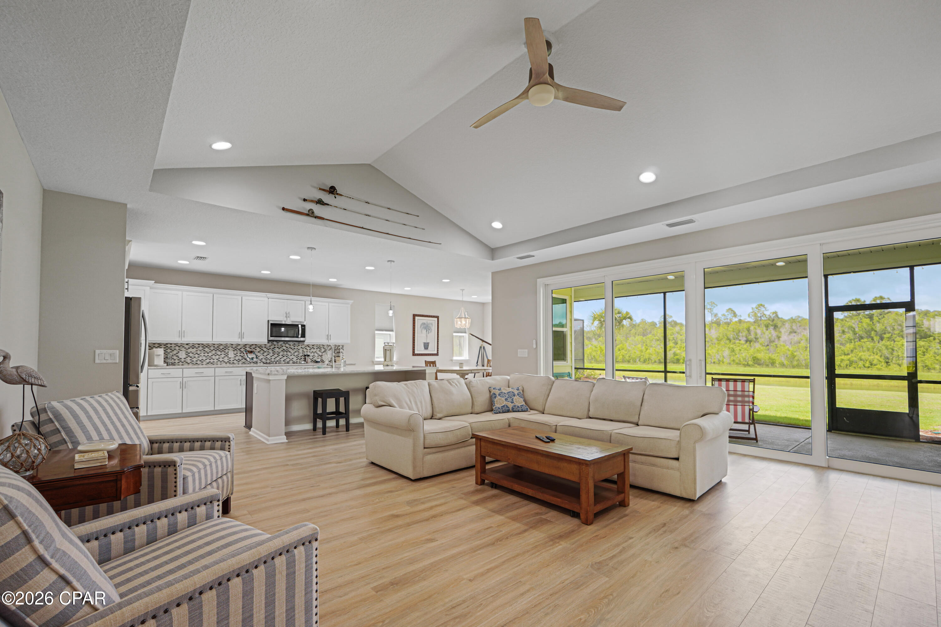 Open-plan living room and kitchen with vaulted ceiling, beige sectional, and sliding doors overlooking a screened patio.