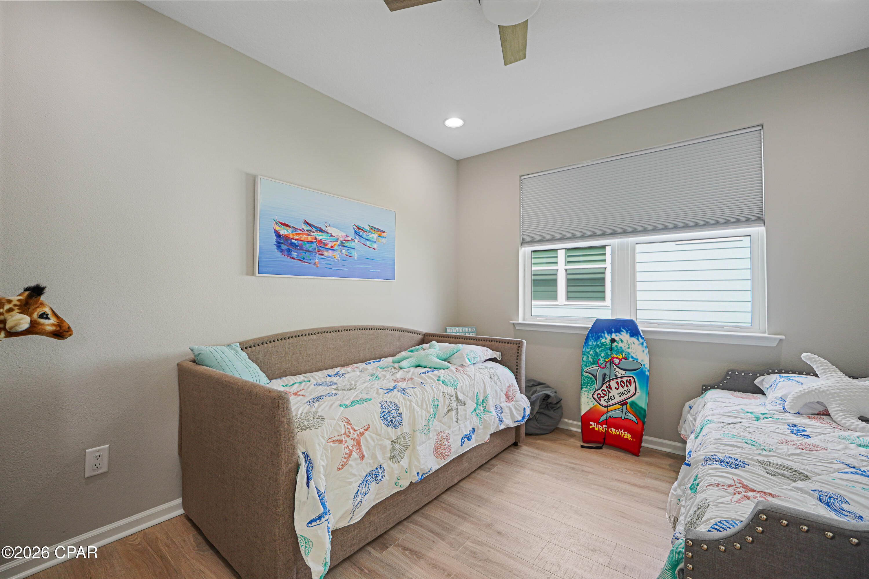 Bedroom with two sea-themed beds and a colorful surfboard beside the window.
