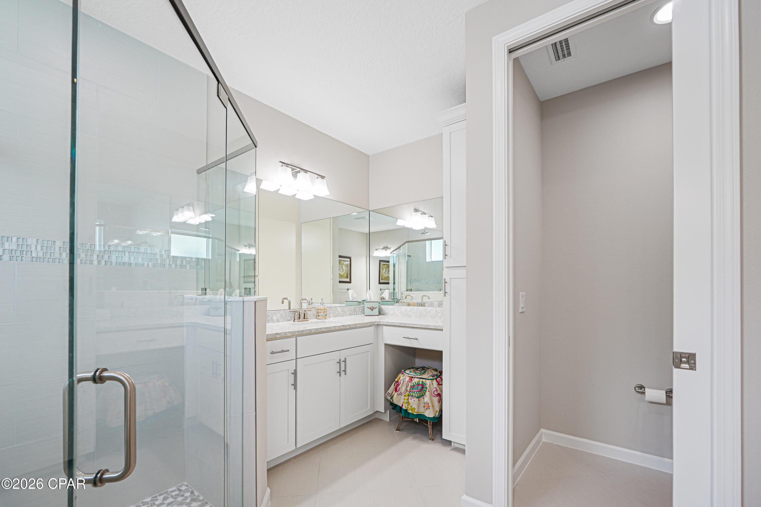 Bathroom with glass shower, mirrored white vanity, and separate toilet alcove.