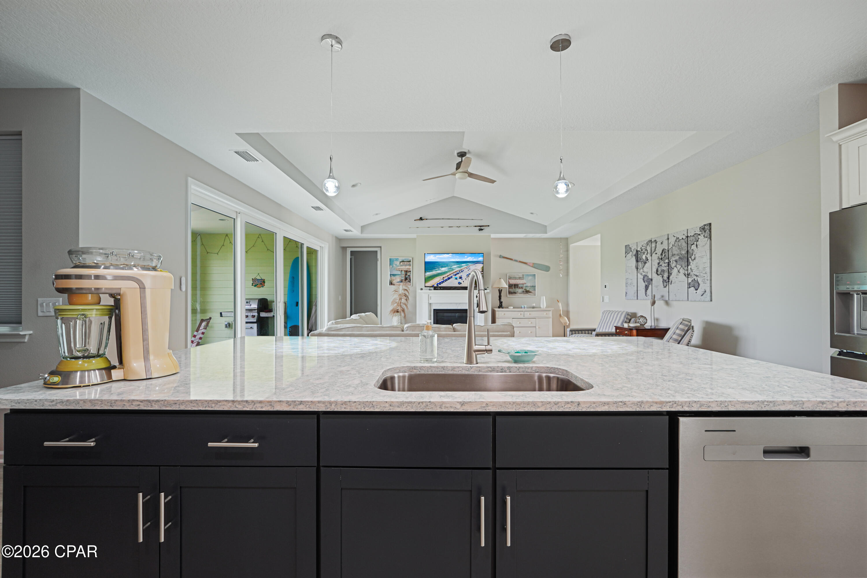 Kitchen island with marble-patterned countertop and dark cabinets, opening onto a vaulted living room.