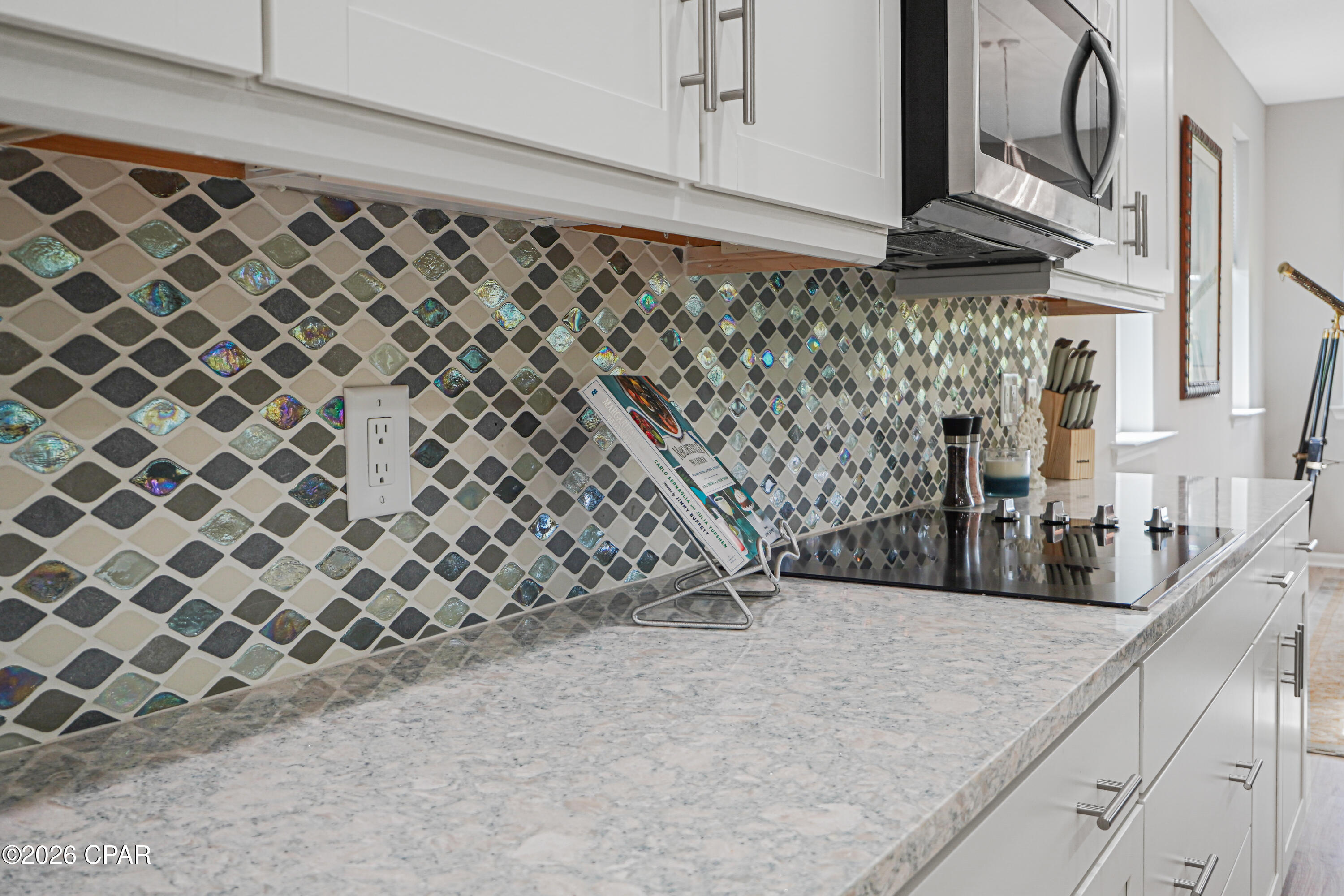 Kitchen with white cabinets, stone counters, stainless appliances, and an iridescent patterned tile backsplash.