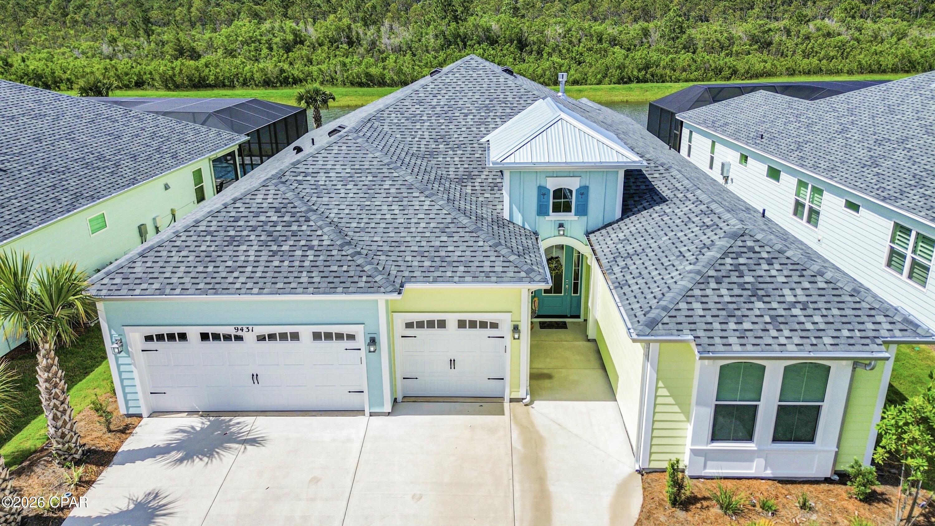 Pastel blue and pale yellow home with a broad gray roof, two garage doors, and a concrete driveway.