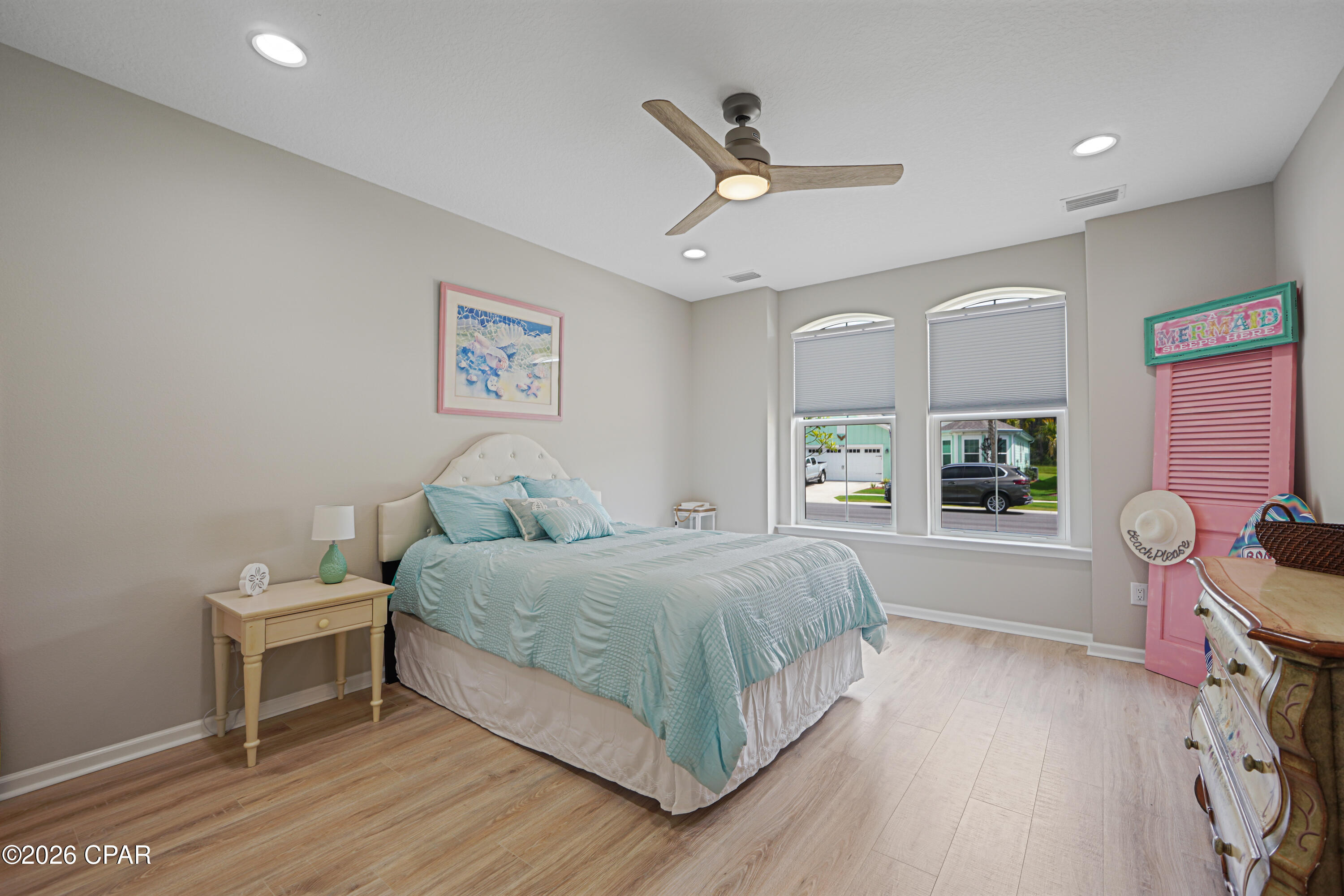 Furnished bedroom with aqua bedding, arched windows, and a wood ceiling fan.