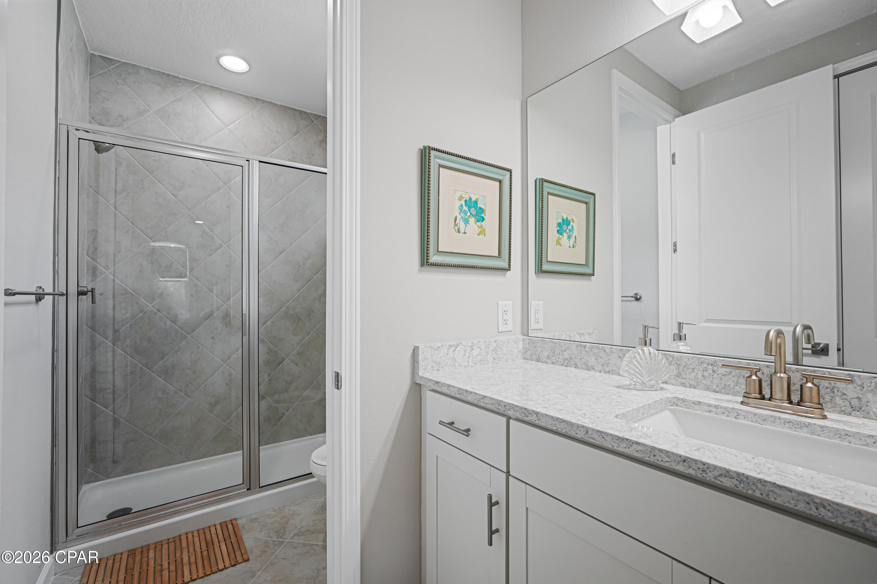 Bathroom with a tiled glass shower and white vanity topped with granite.