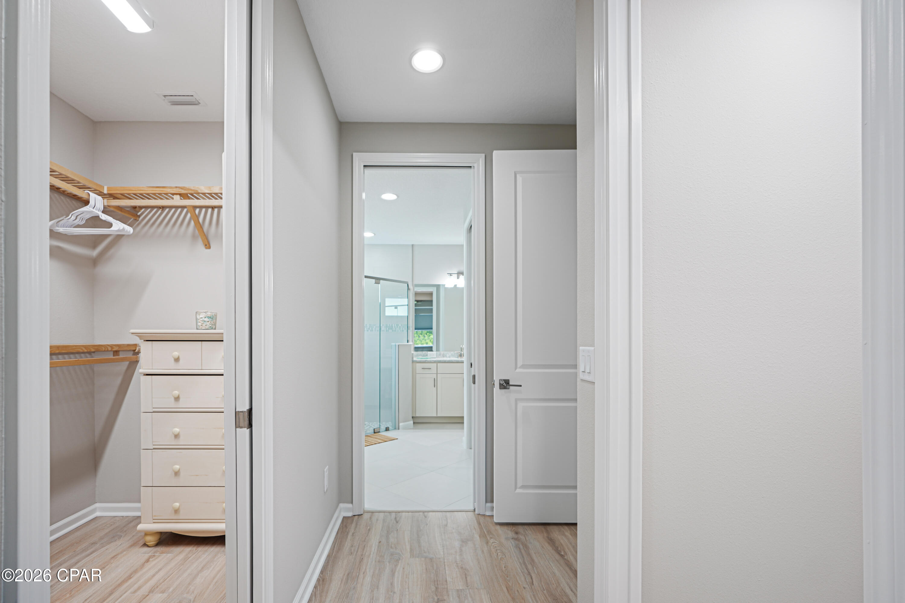 Hallway with an open closet and a view through to a bathroom with a glass shower.