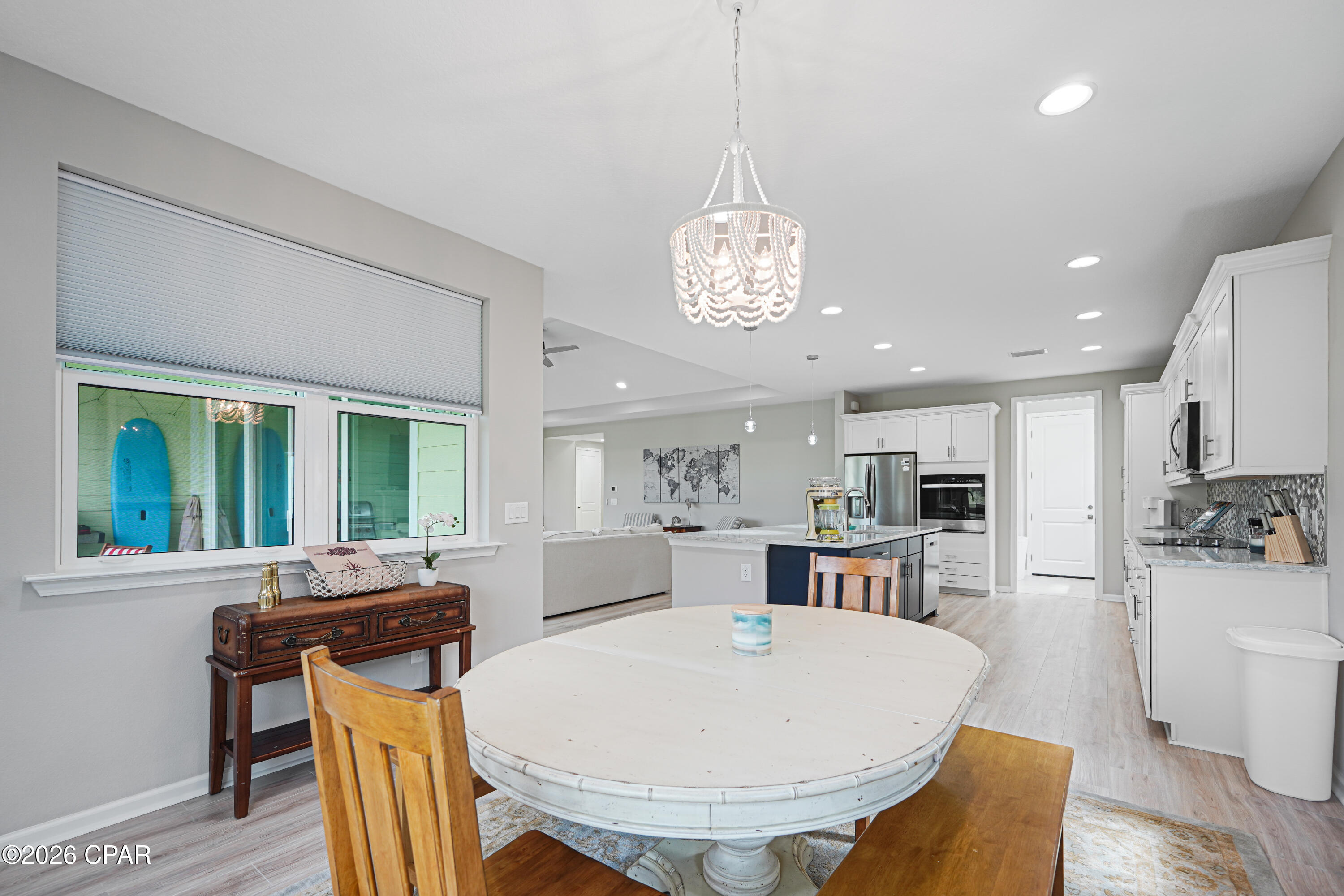 Open-plan kitchen and dining area with a white island, oval table, and beaded chandelier.