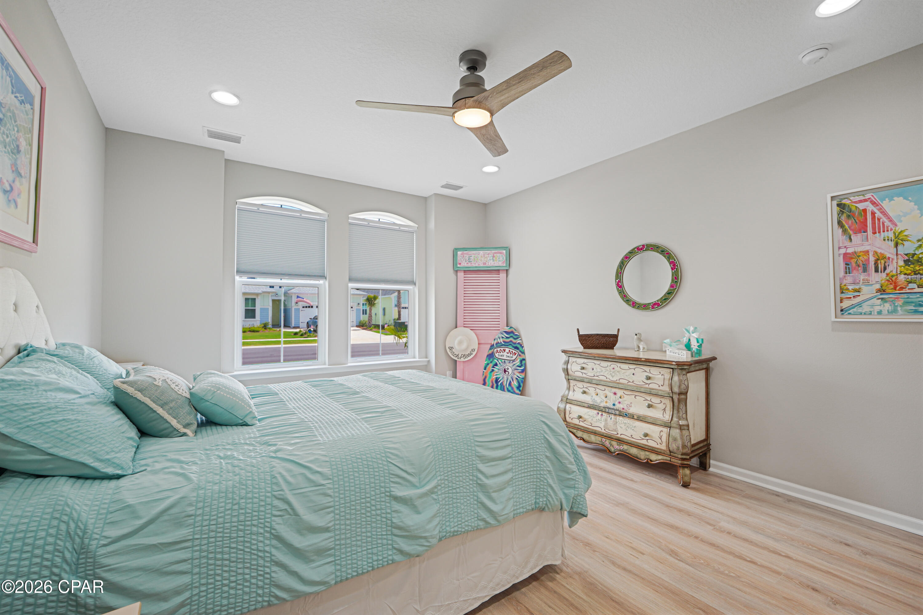 Bedroom with aqua bedding, arched windows, a ceiling fan, and a painted coastal-style dresser.
