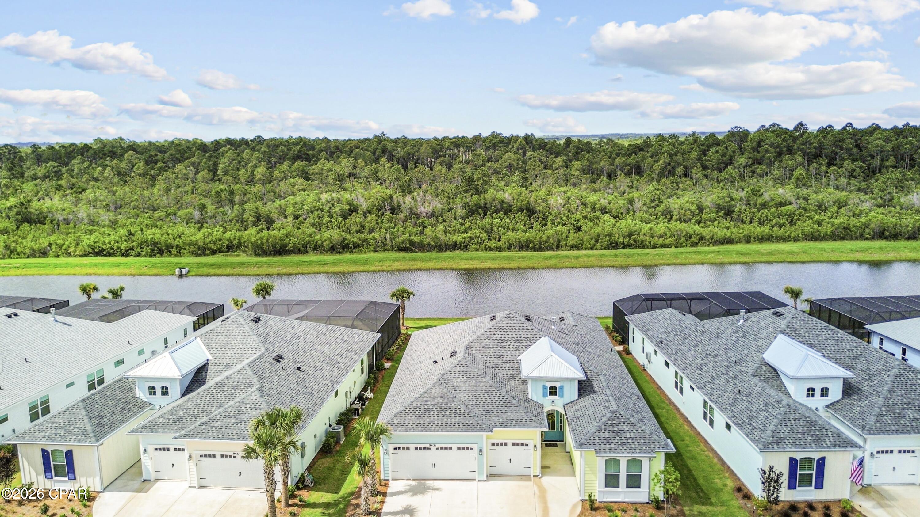 Aerial view of 9431 Paradise Drive beside a pond, with neighboring homes and a wooded greenbelt.