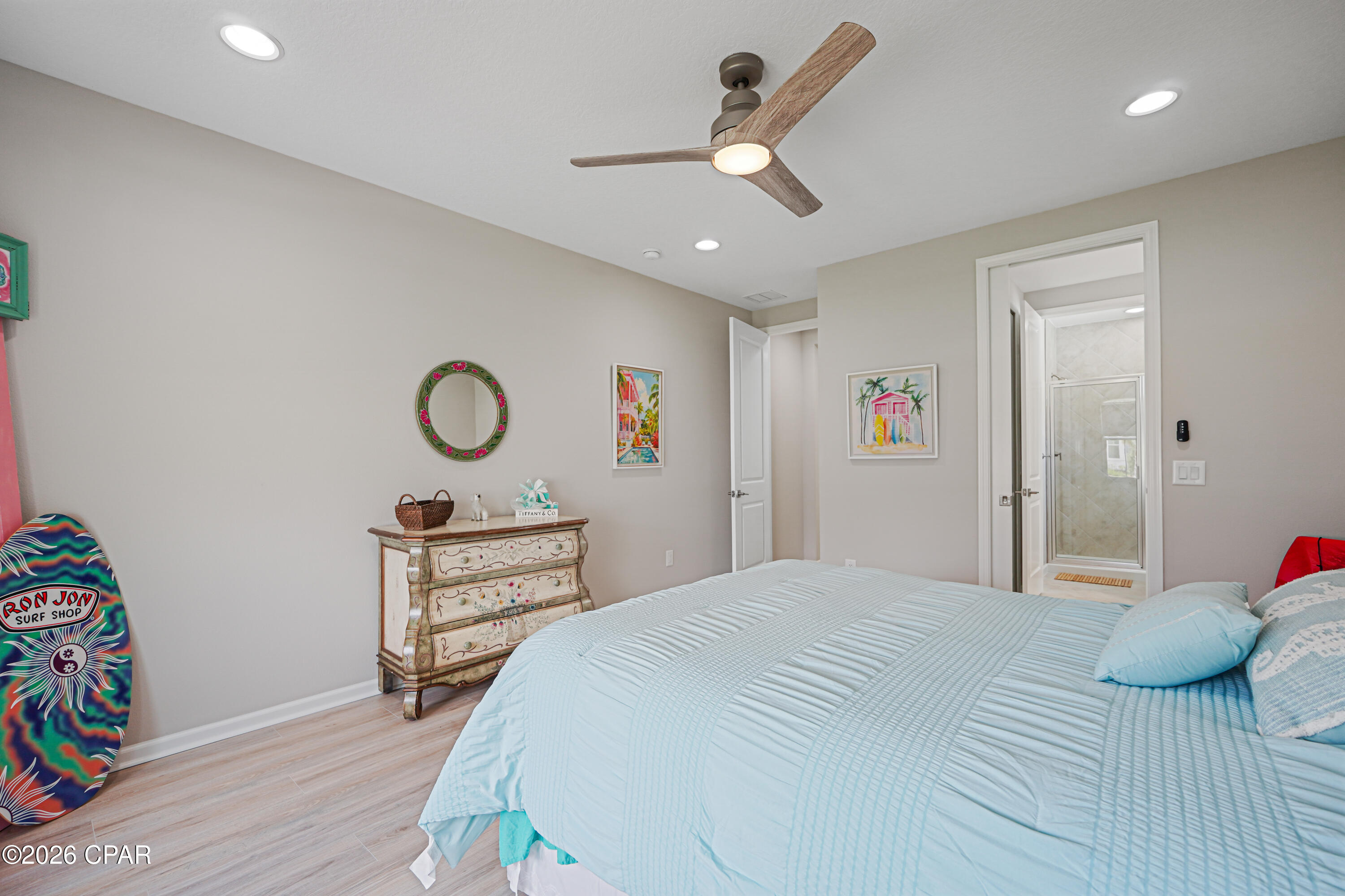 Bedroom with light blue bedding, a painted dresser, and a doorway to a tiled shower.