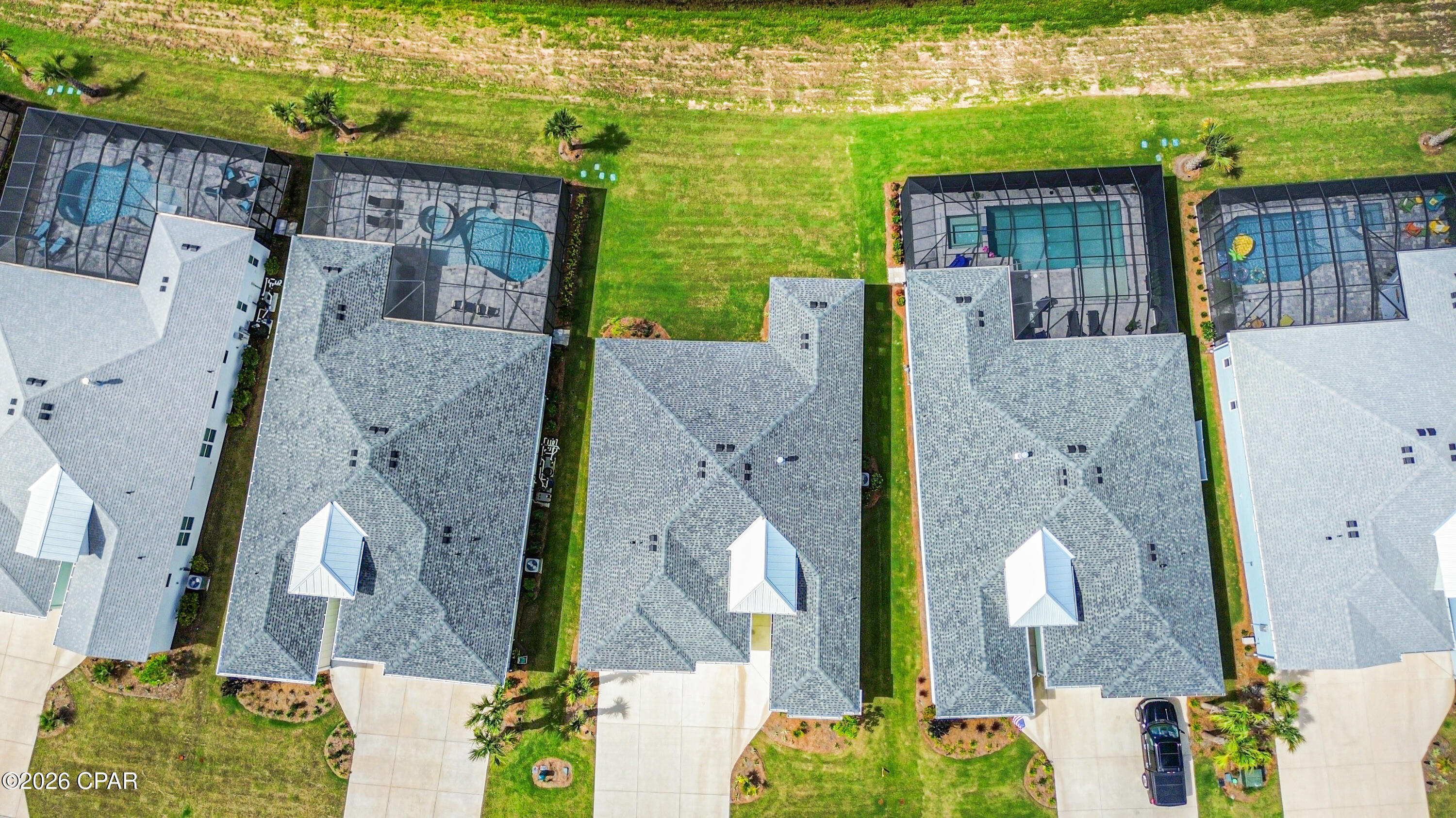 Aerial view of homes with gray roofs, green lawns, and screened backyard pools.