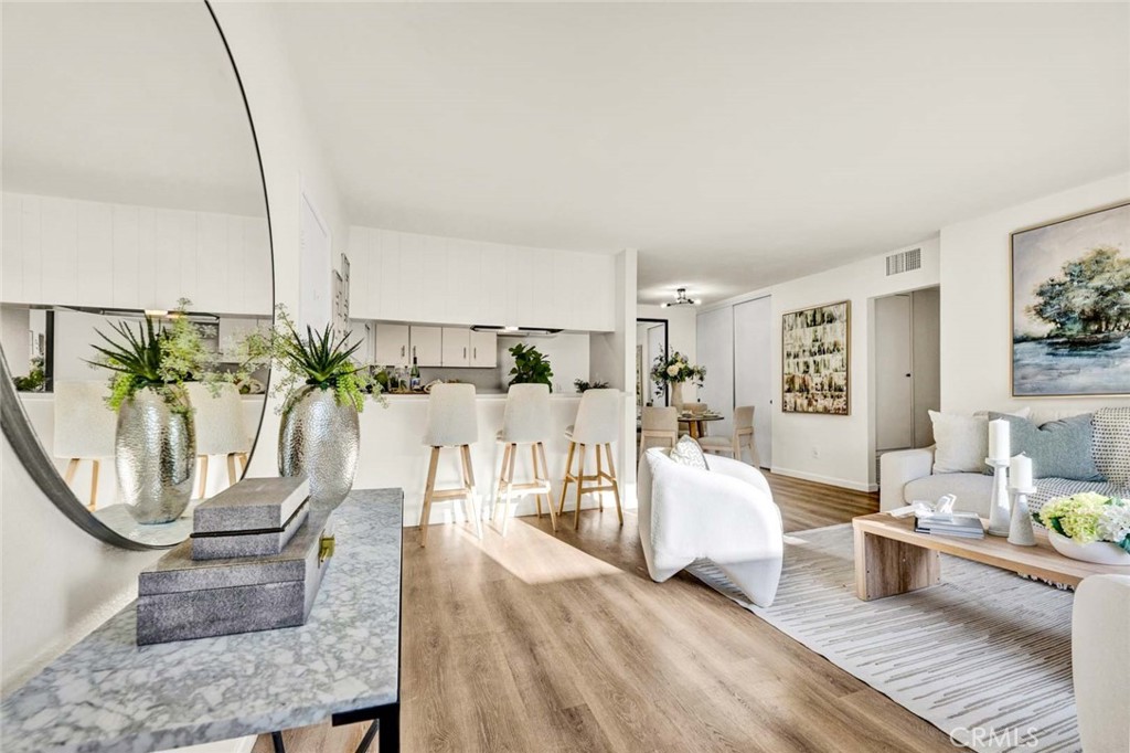 Staged open-plan living room and kitchen with a breakfast bar, white cabinetry, and wood-look floors.
