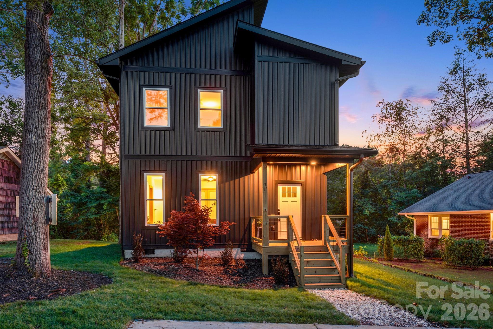Modern dark-sided two-story home with a lit front porch at dusk.