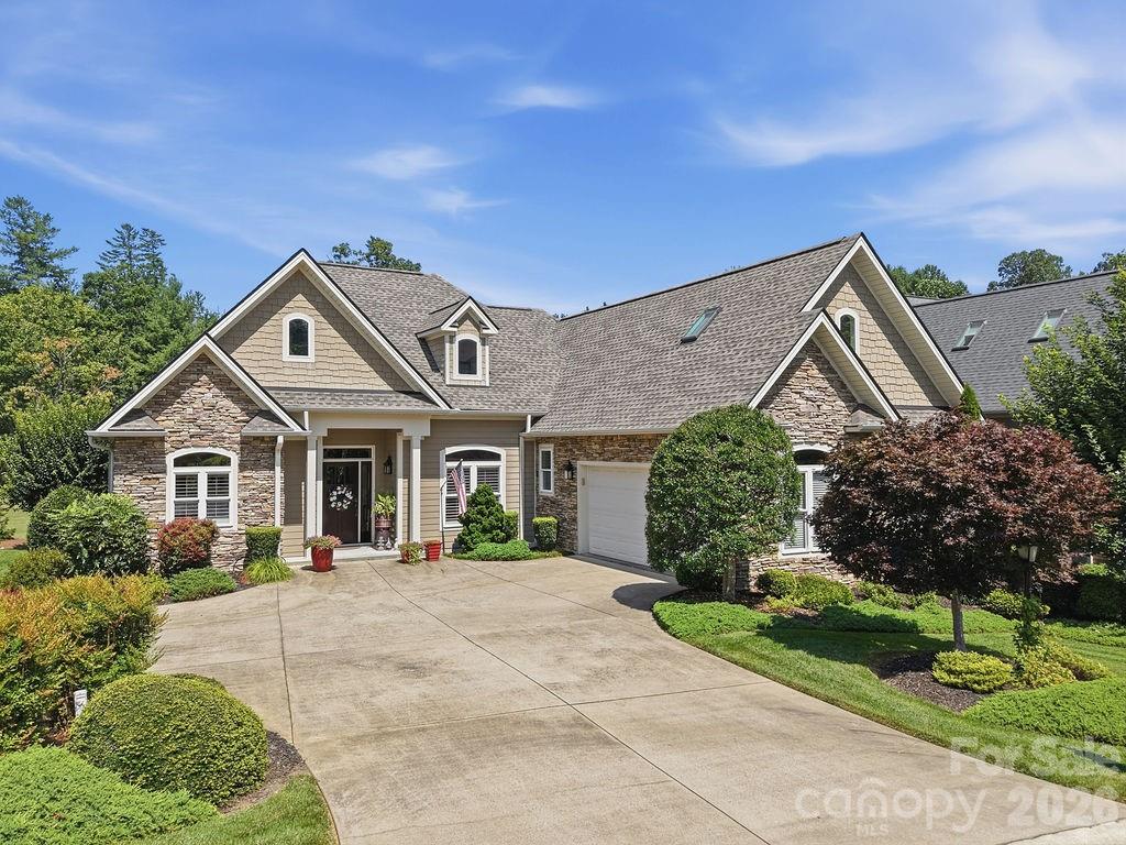 Large beige home with stone accents, multiple gables, a garage, and a landscaped driveway.