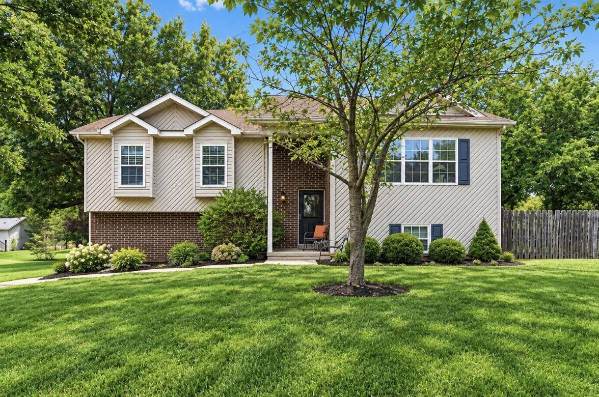 Split-level home with cream siding, brick accents, and a broad green lawn.