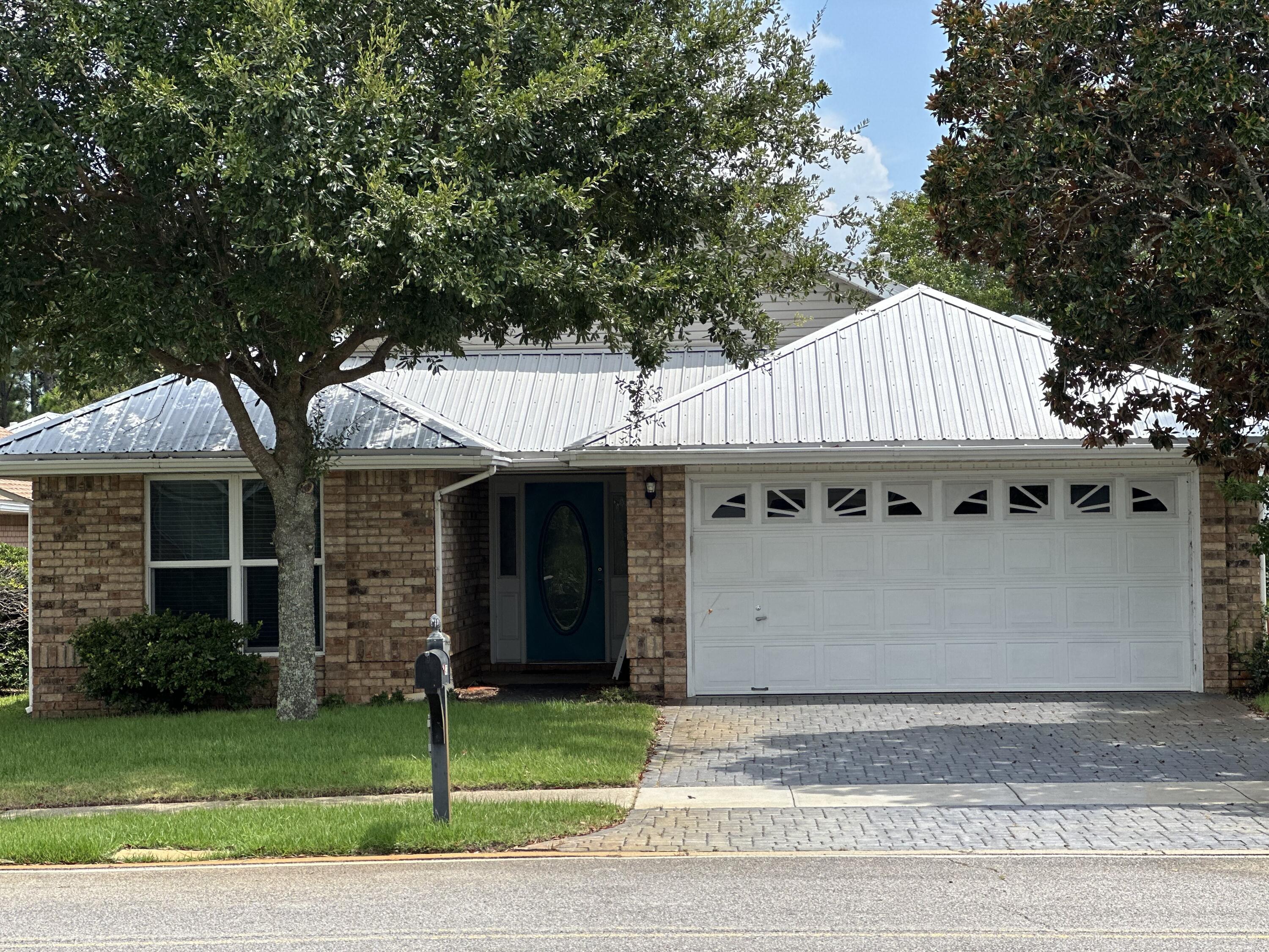 Brick house with a light metal roof, white double garage, and mature trees shading the front lawn.