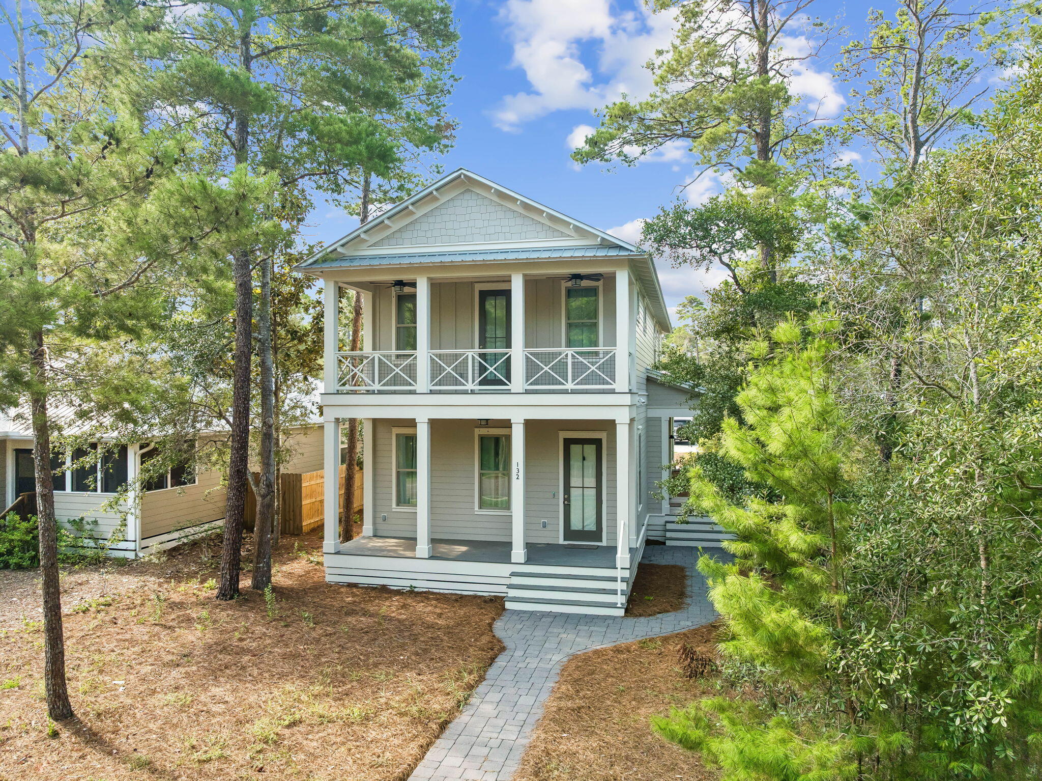 Two-story gray home with covered porches and a curved paver walkway.