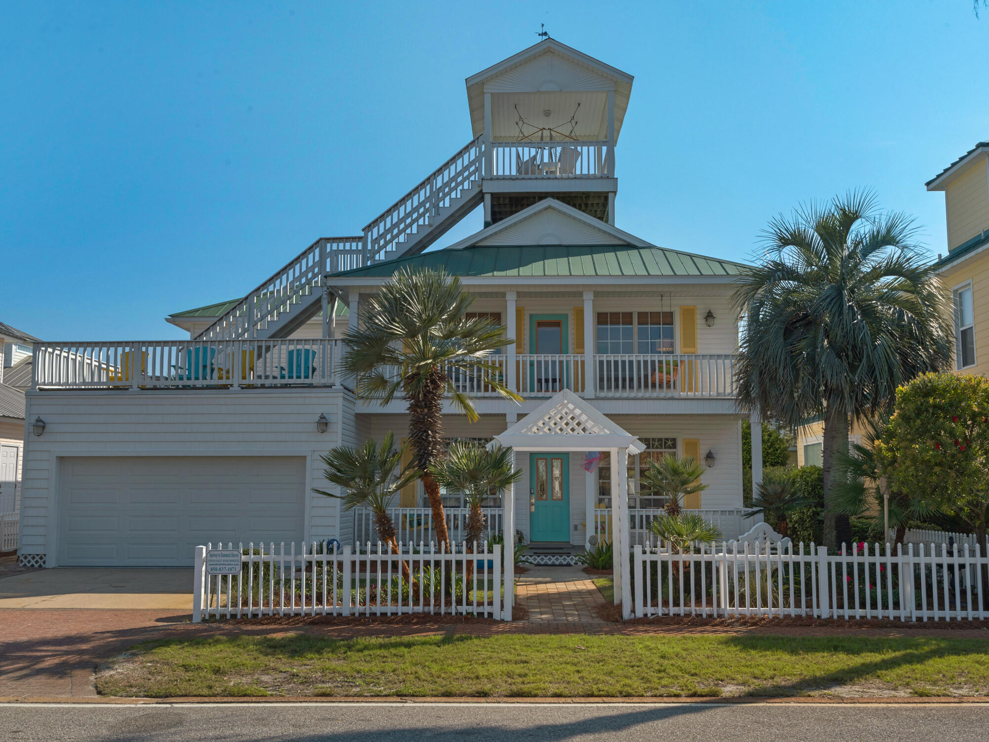 Coastal-style house with a rooftop deck, exterior stairs, palm trees, and a turquoise front door.