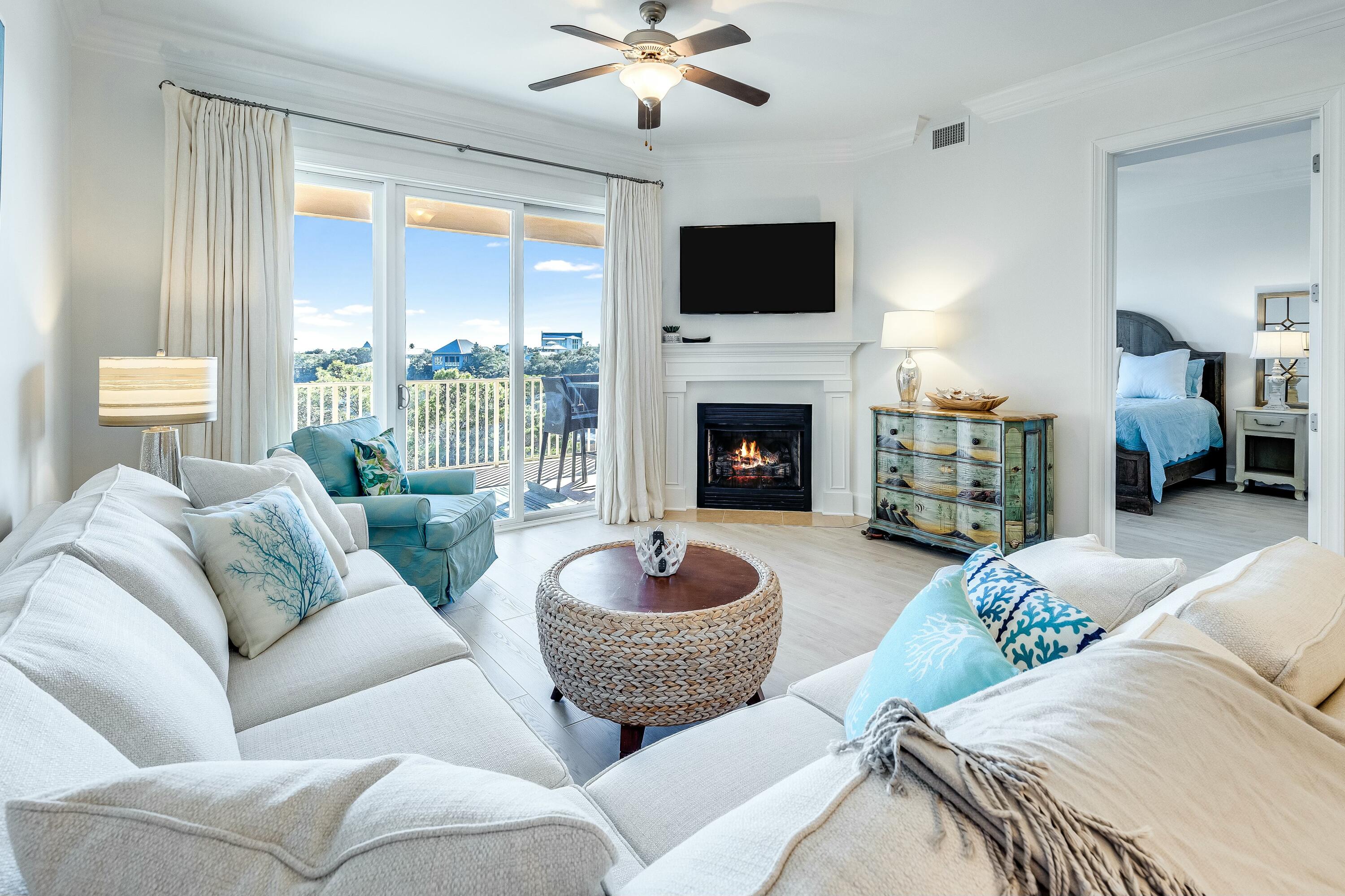 Living room with a fireplace, white sofas, and sliding doors opening to a balcony with coastal views.