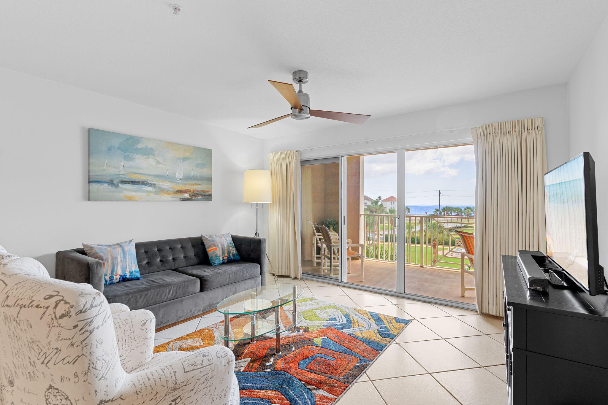 Furnished condo living room with sliding doors to a balcony overlooking the ocean.