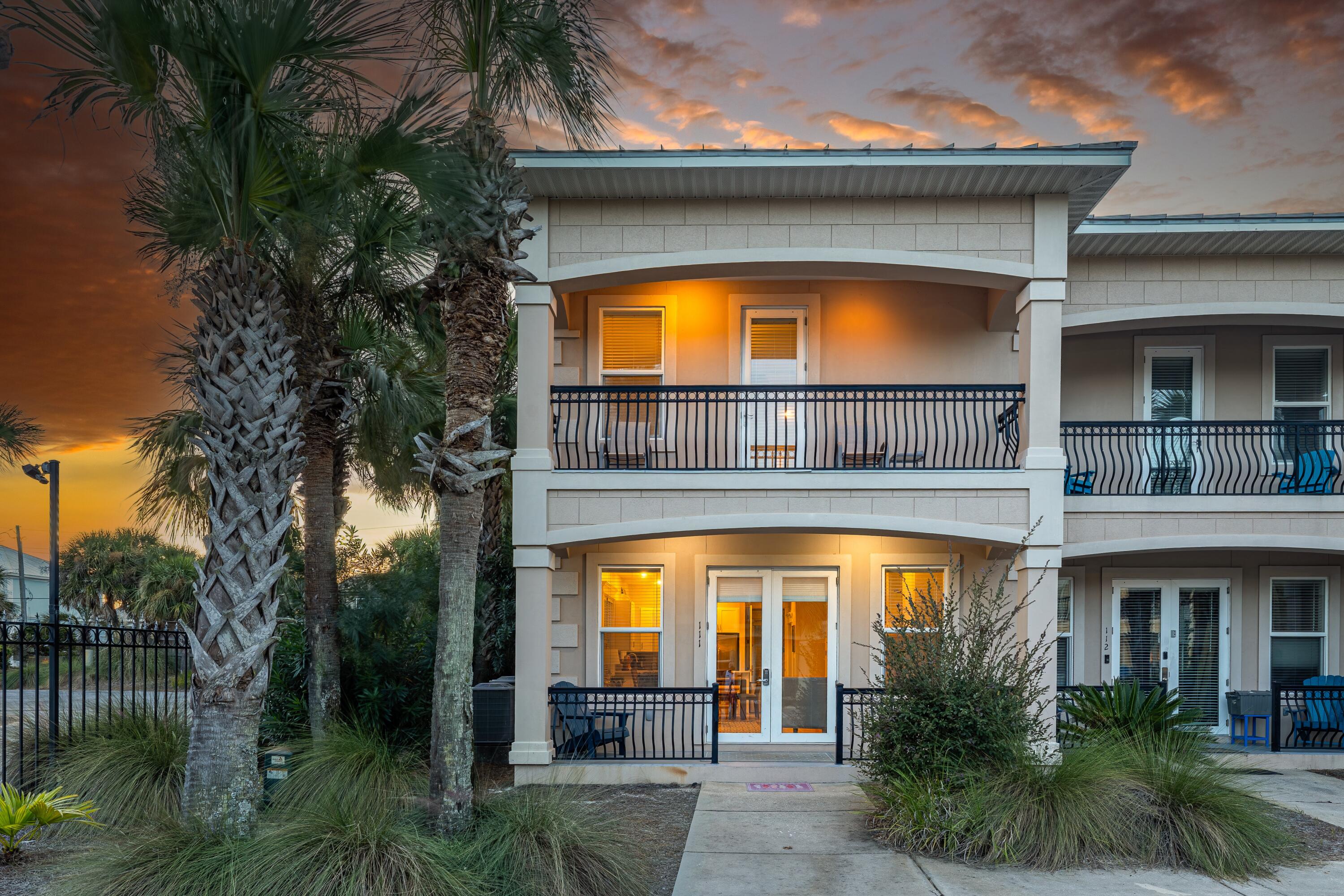 Coastal residence with two-story balconies and palm trees at sunset.