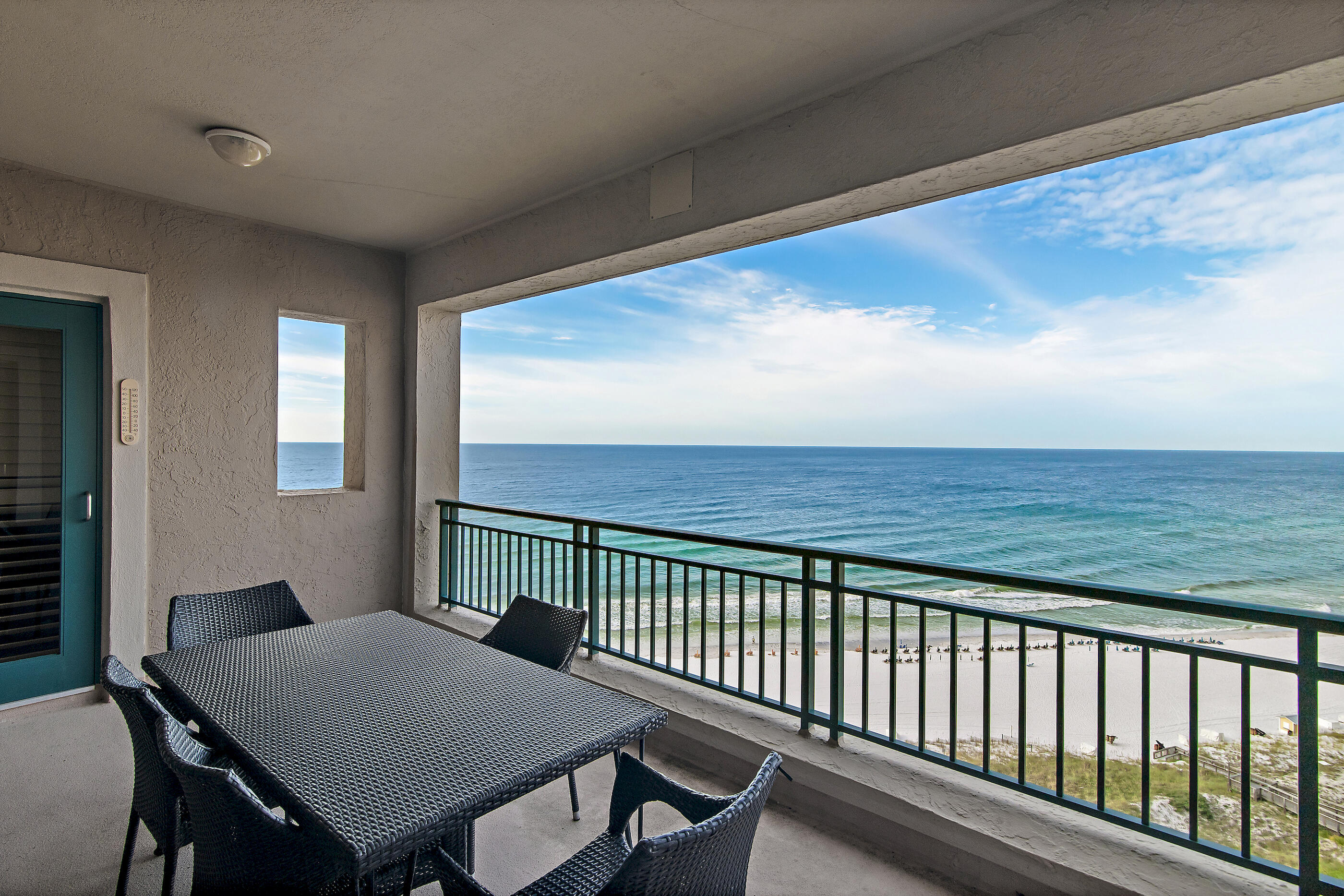 Covered condo balcony with a woven dining table overlooking the ocean and beach.