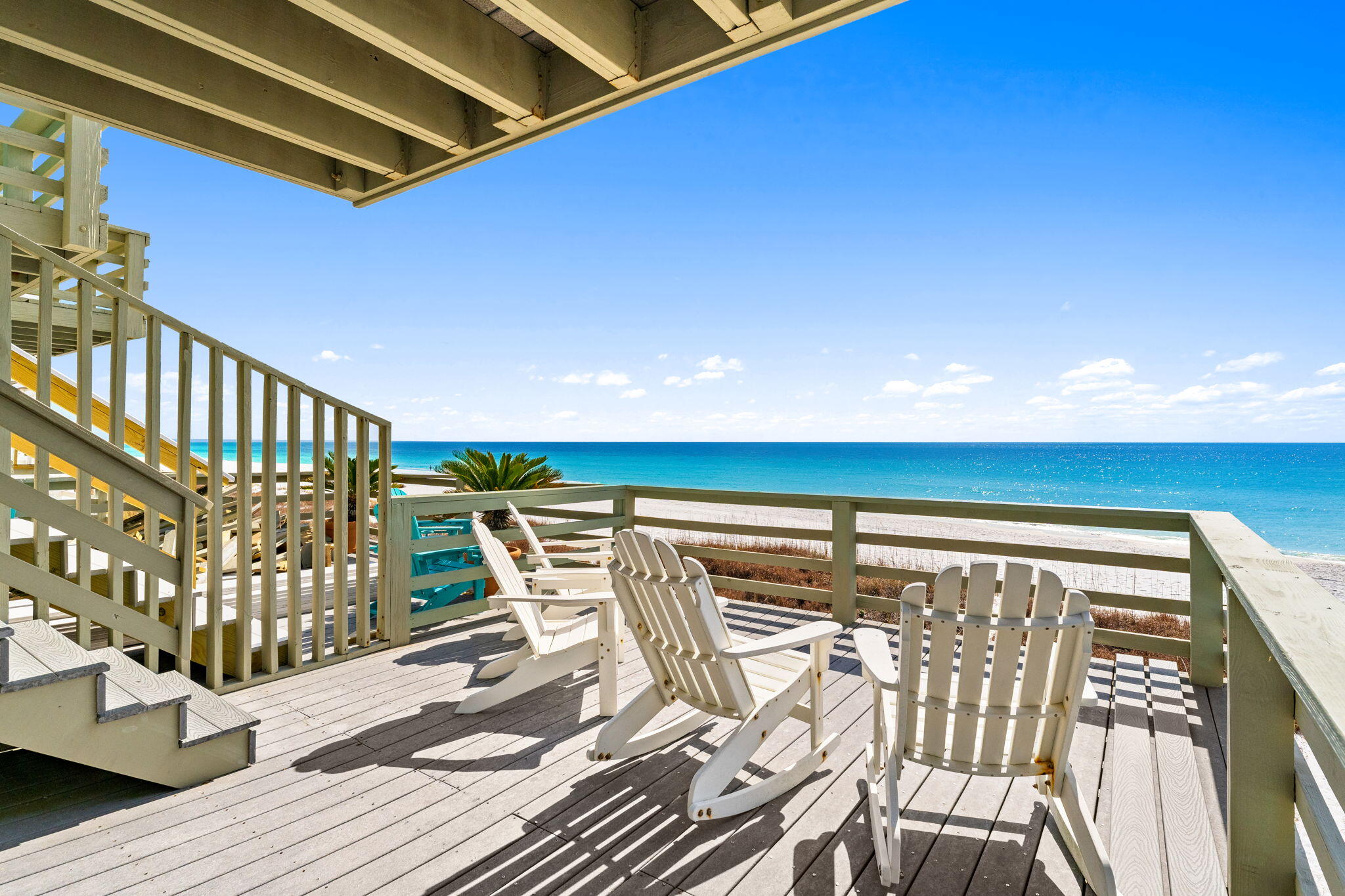 Beachfront deck with white Adirondack chairs overlooking the Gulf and sandy beach.