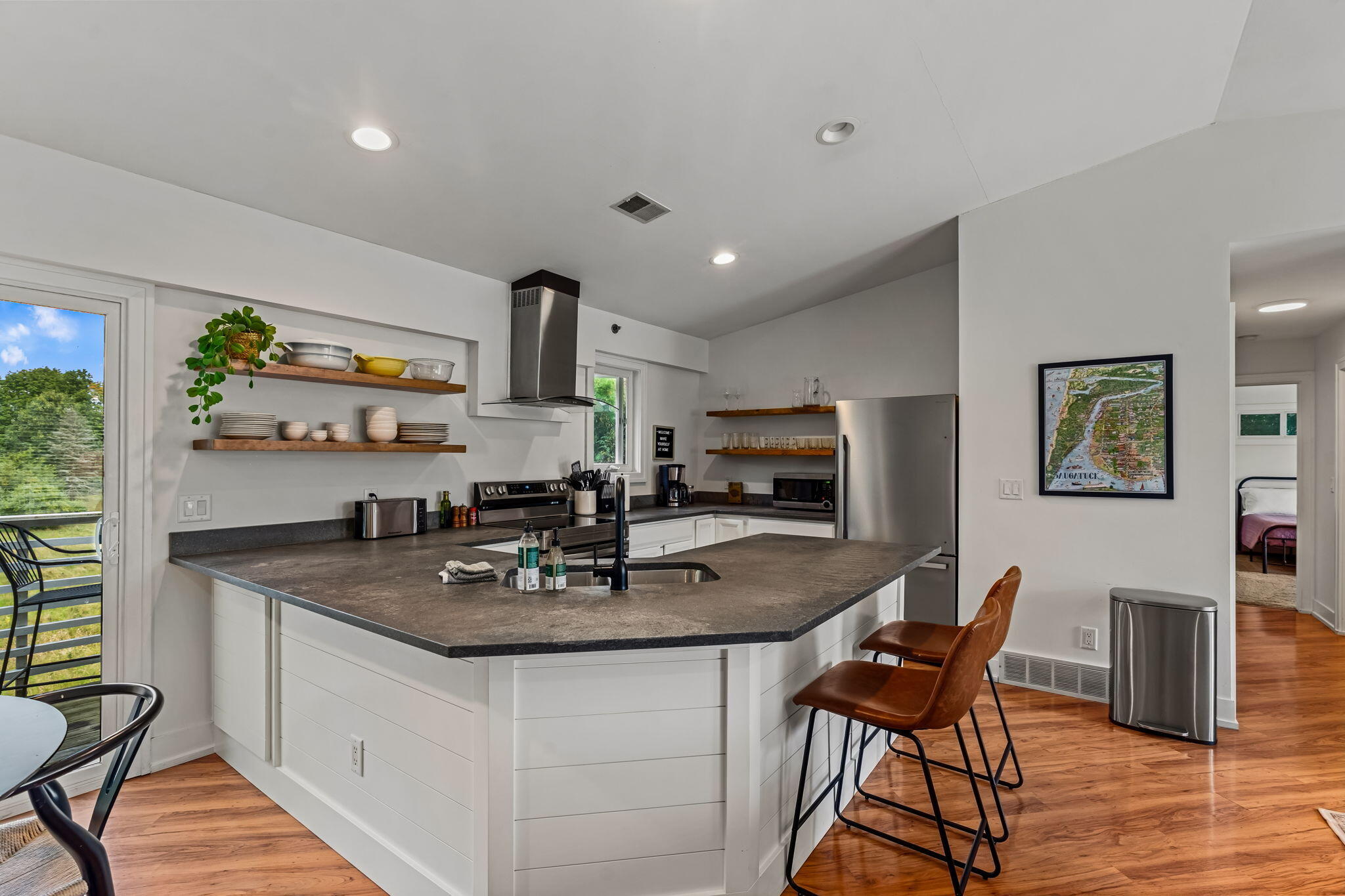 Kitchen with a large gray island, open wood shelves, stainless appliances, and a framed Saugatuck map.