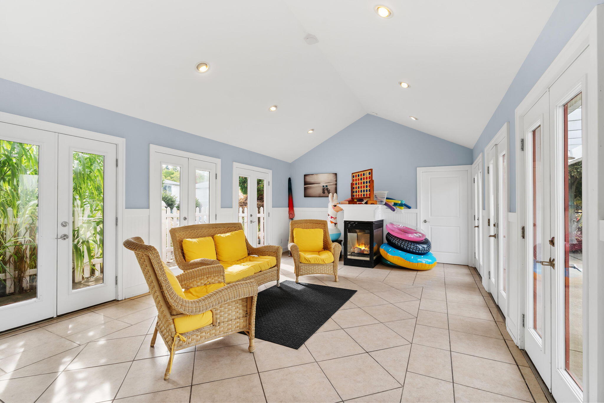 Sunroom with wicker seating and yellow cushions, tiled floor, glass doors, a small fireplace, and pool floats.