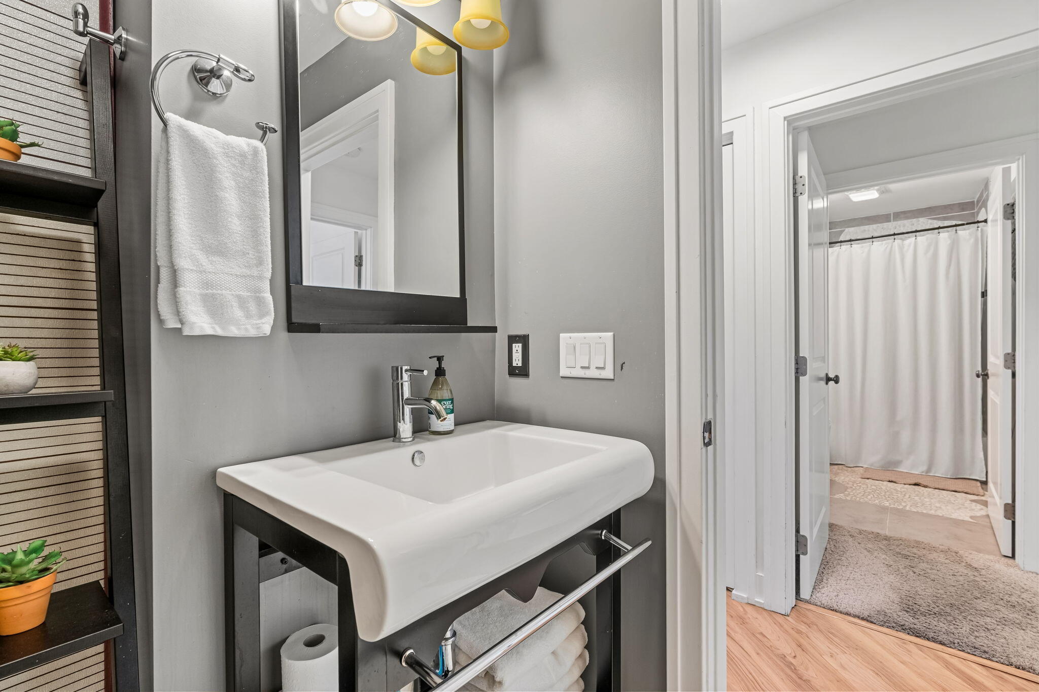 Bathroom with a white vessel sink and dark vanity, opening to a shower with a white curtain.
