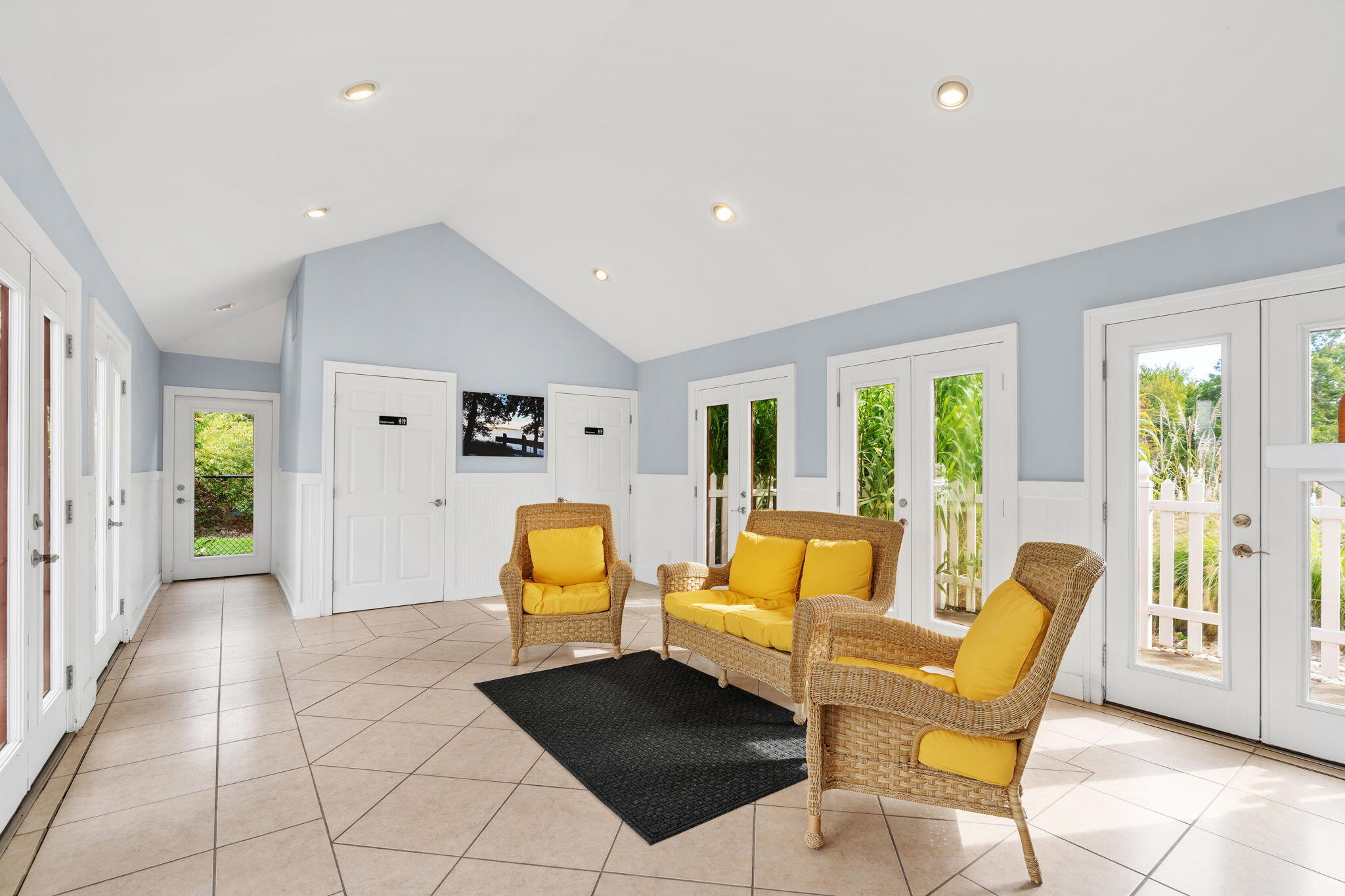 Sunroom with wicker seating, yellow cushions, and glass doors overlooking greenery.