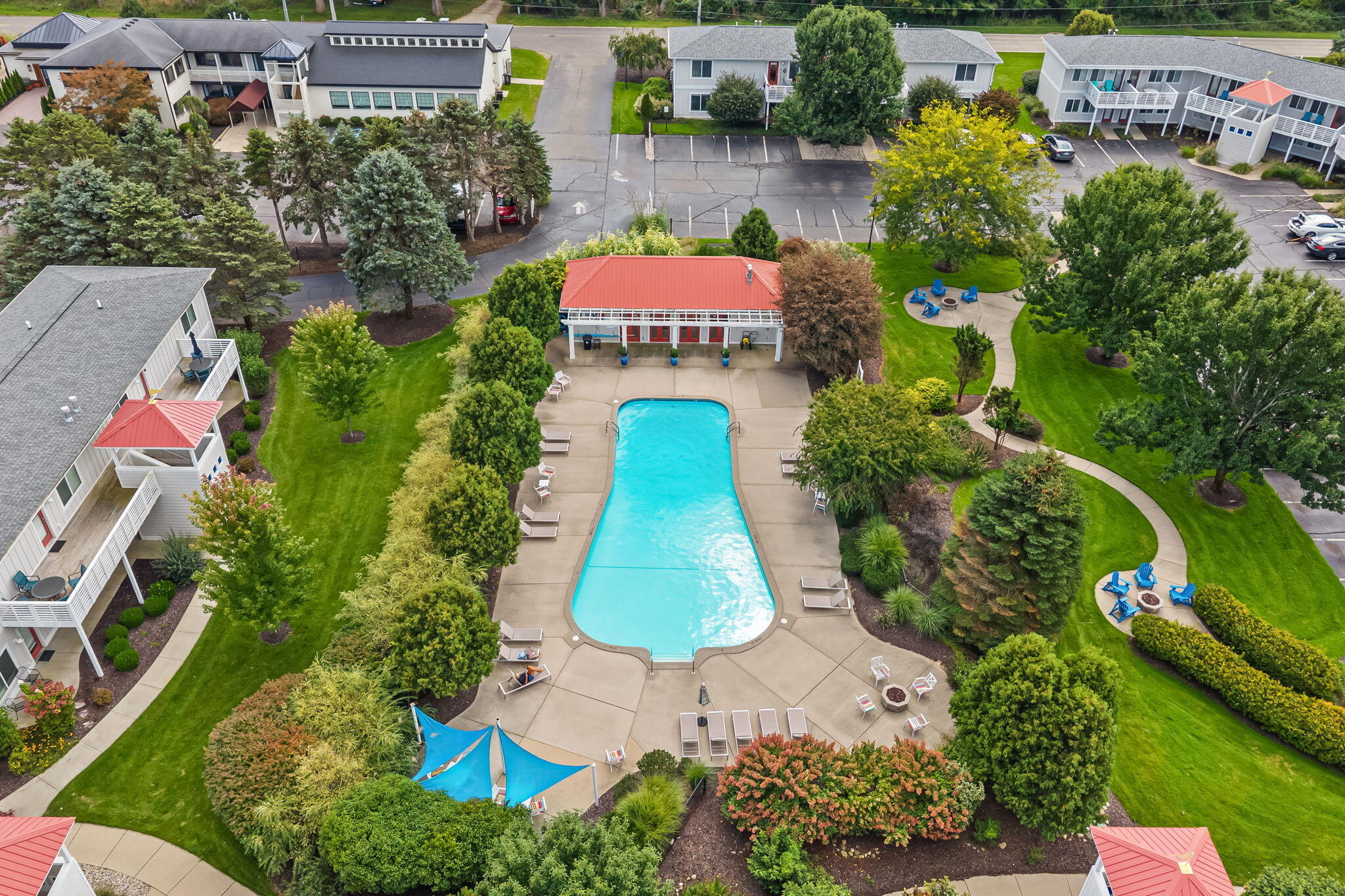 Aerial view of a condominium pool courtyard with a red-roofed pool house and landscaped paths.