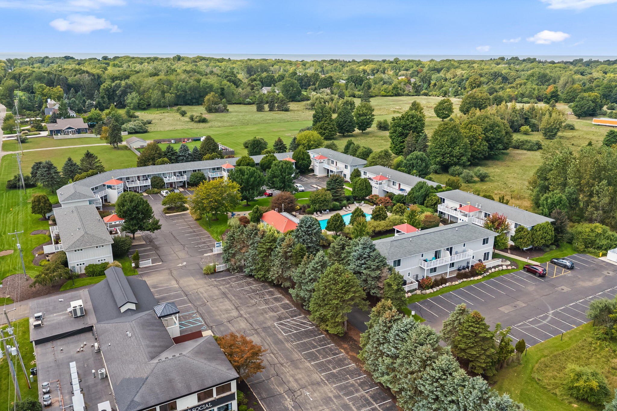 Aerial view of a residential complex with a central pool, landscaped grounds, and large parking lots.