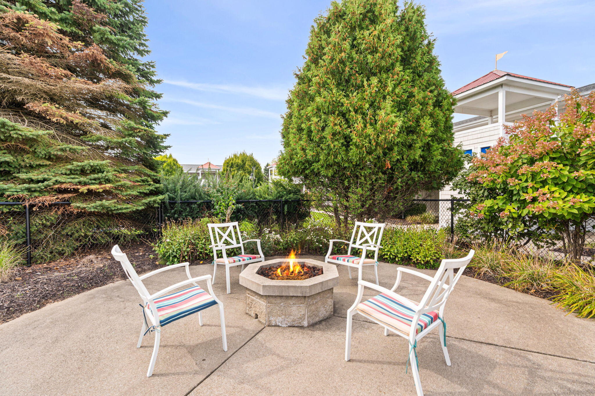 Outdoor patio with a stone fire pit, four striped-cushion chairs, and a covered porch nearby.