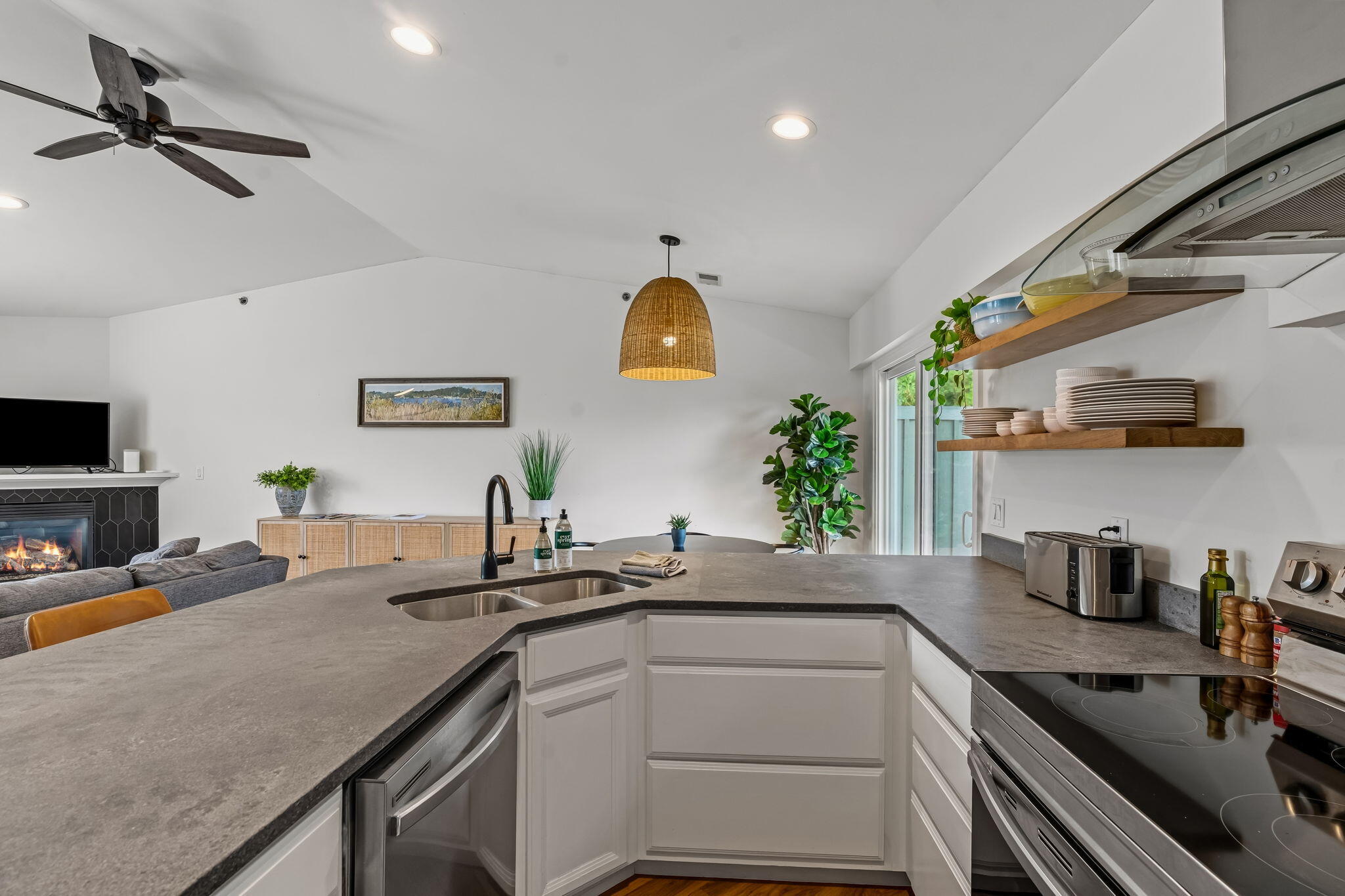 Modern kitchen with a broad gray island, open wood shelves, and a living area with fireplace.