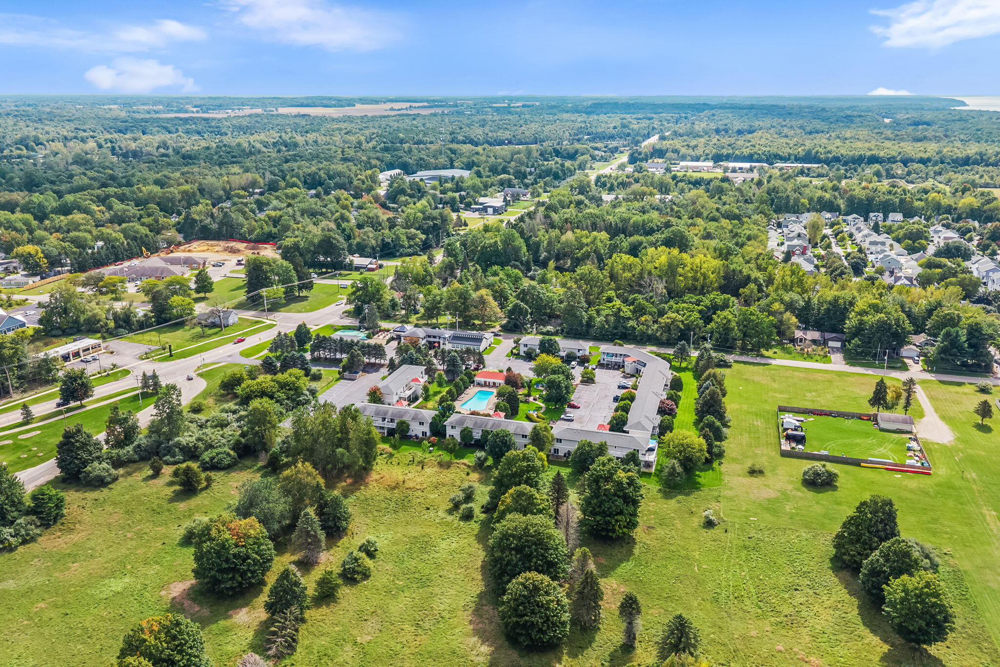 Aerial view of a low-rise property with a central pool, broad lawns, and surrounding woods.