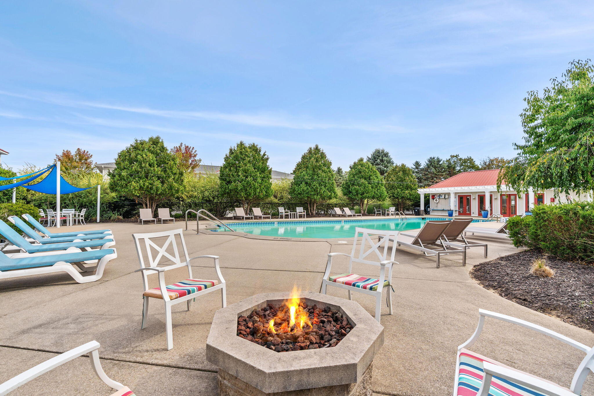 Outdoor pool patio with a lit stone fire pit and colorful cushioned chairs.