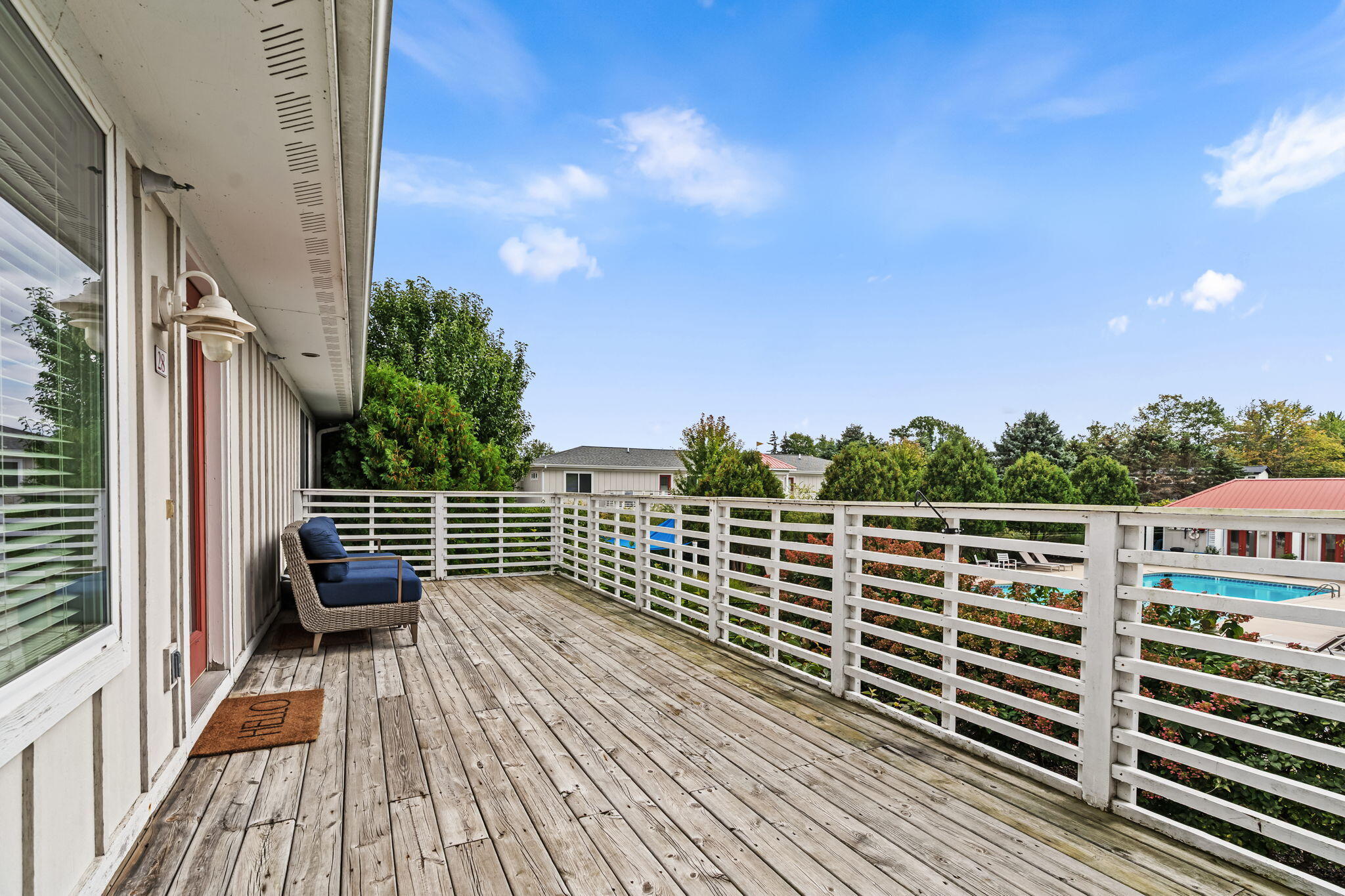 Wood deck with white railings, a blue-cushioned chair, and a swimming pool beyond.