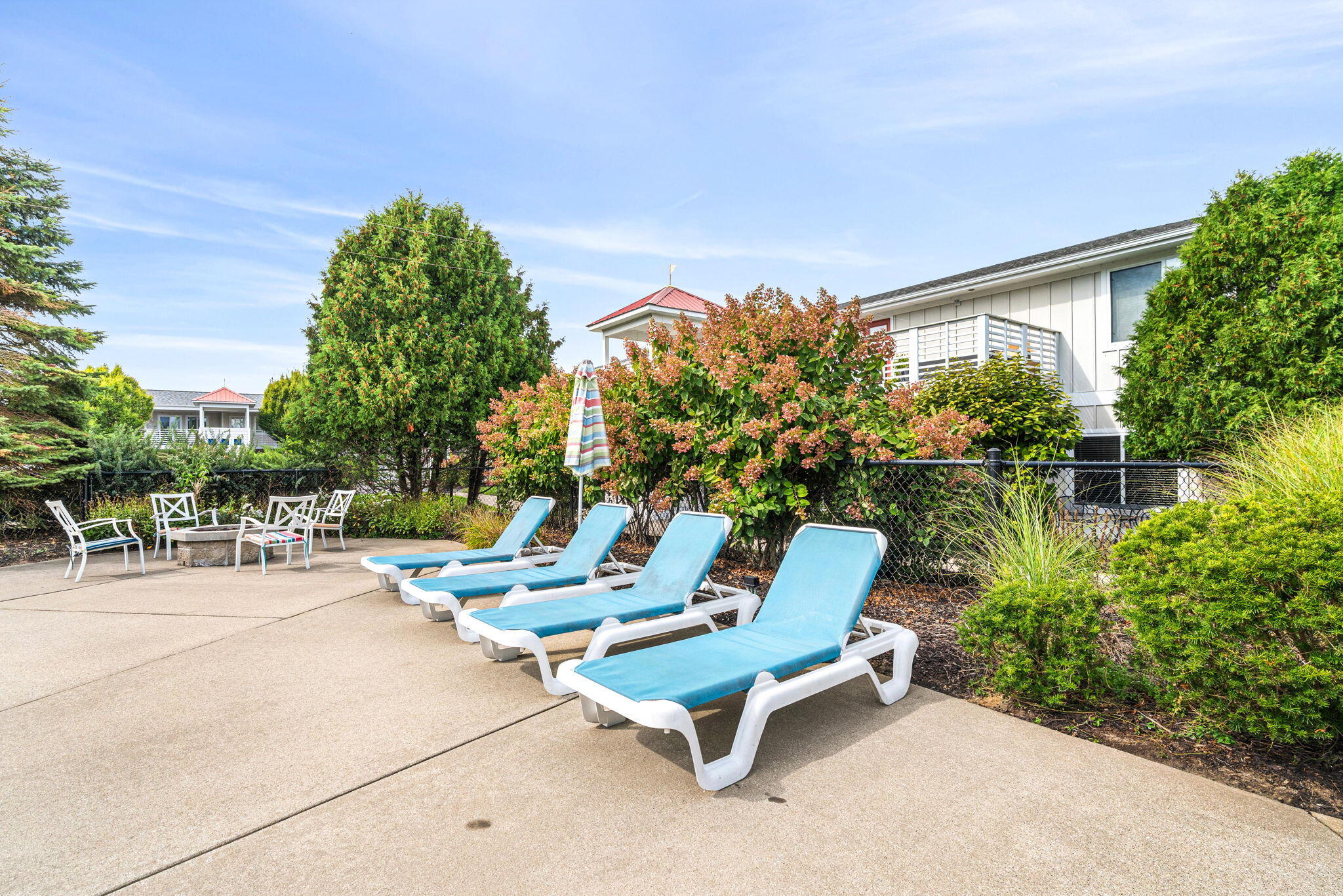 Patio with blue-cushioned loungers, a white outdoor dining set, and flowering shrubs beside the home.