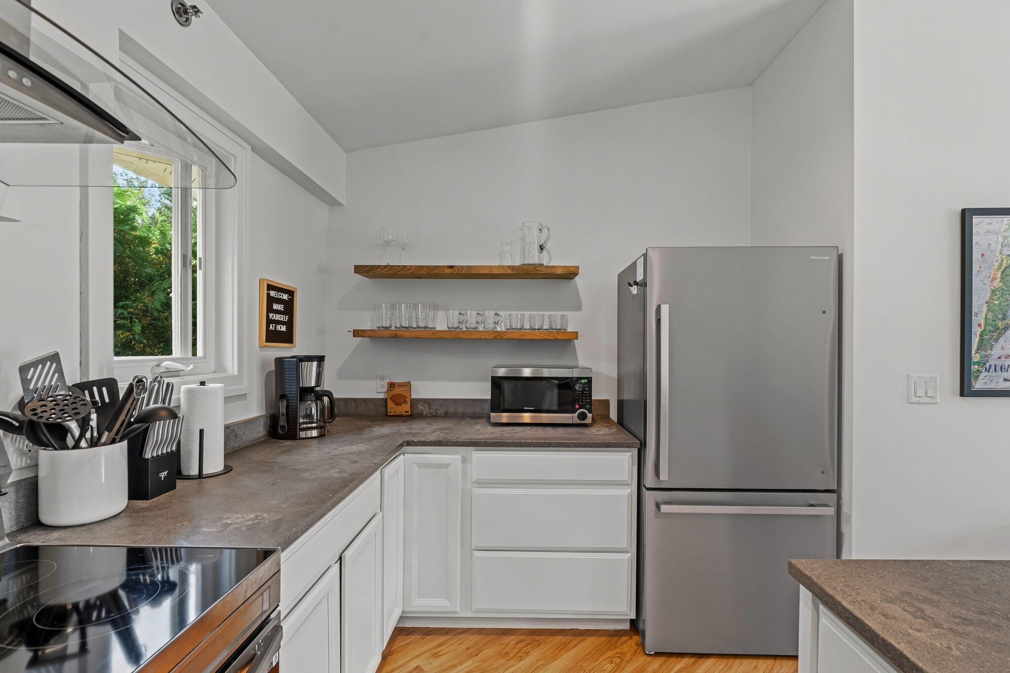 Kitchen with white cabinets, gray counters, wooden shelves, and a stainless-steel refrigerator.