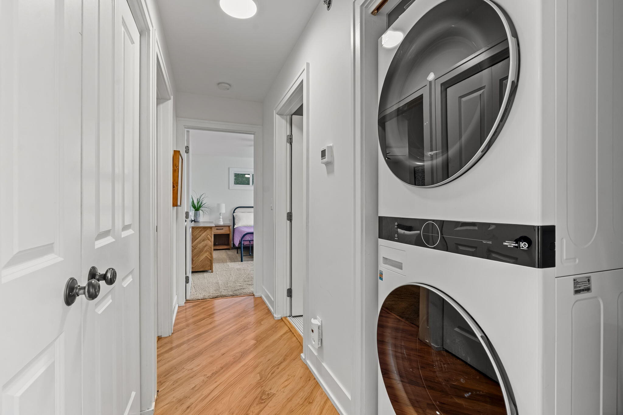 Hallway with stacked washer and dryer, wood flooring, and a bedroom visible through the doorway.