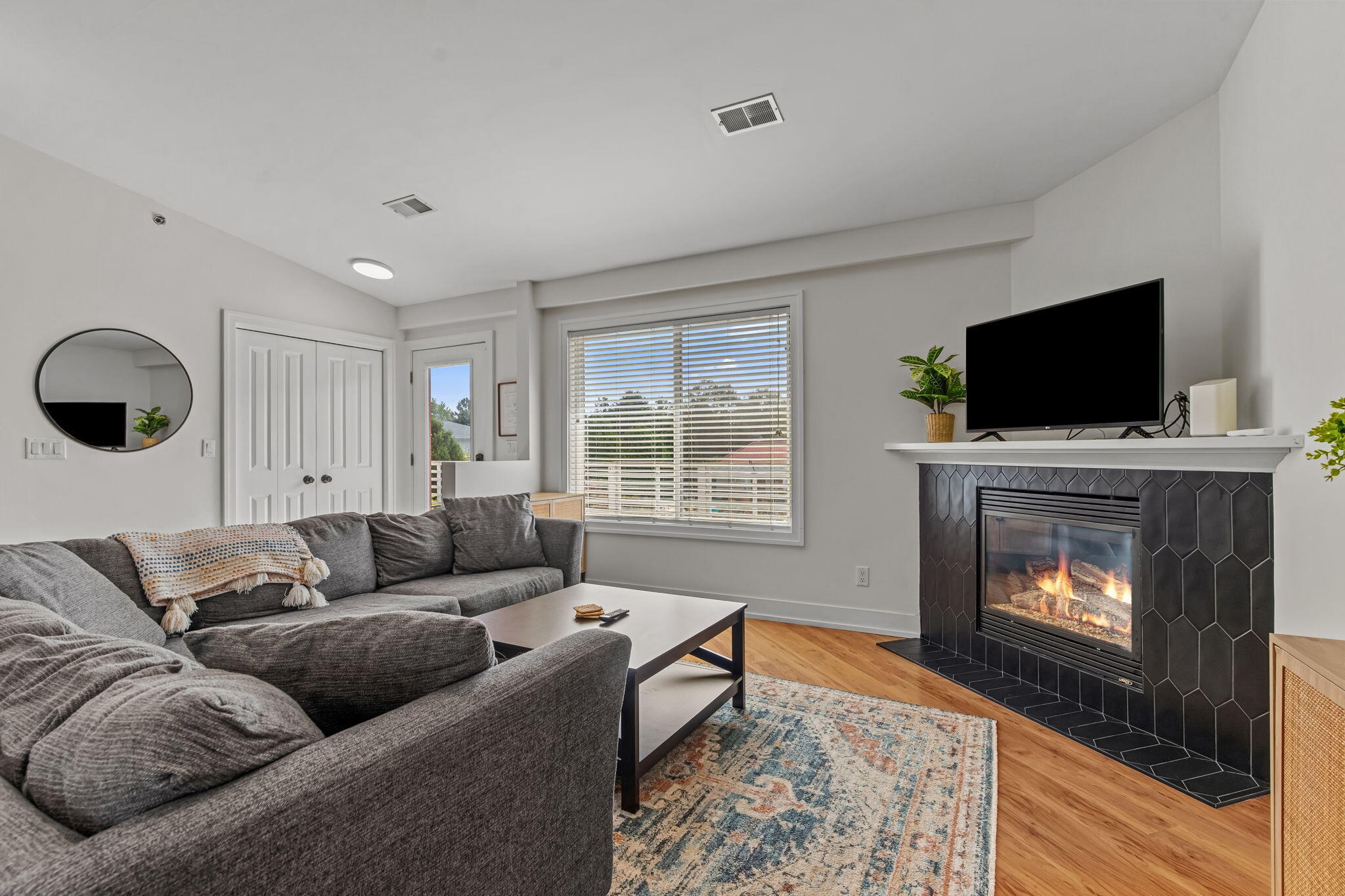 Living room with a gray sectional and a lit fireplace framed by dark hexagonal tile.