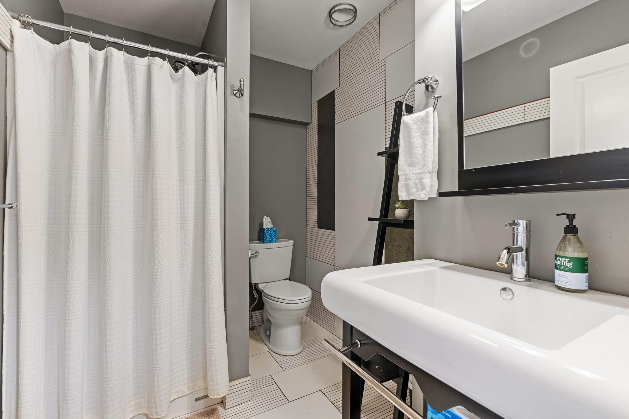Modern bathroom with a large white sink, chrome faucet, curtained shower, and patterned tile.