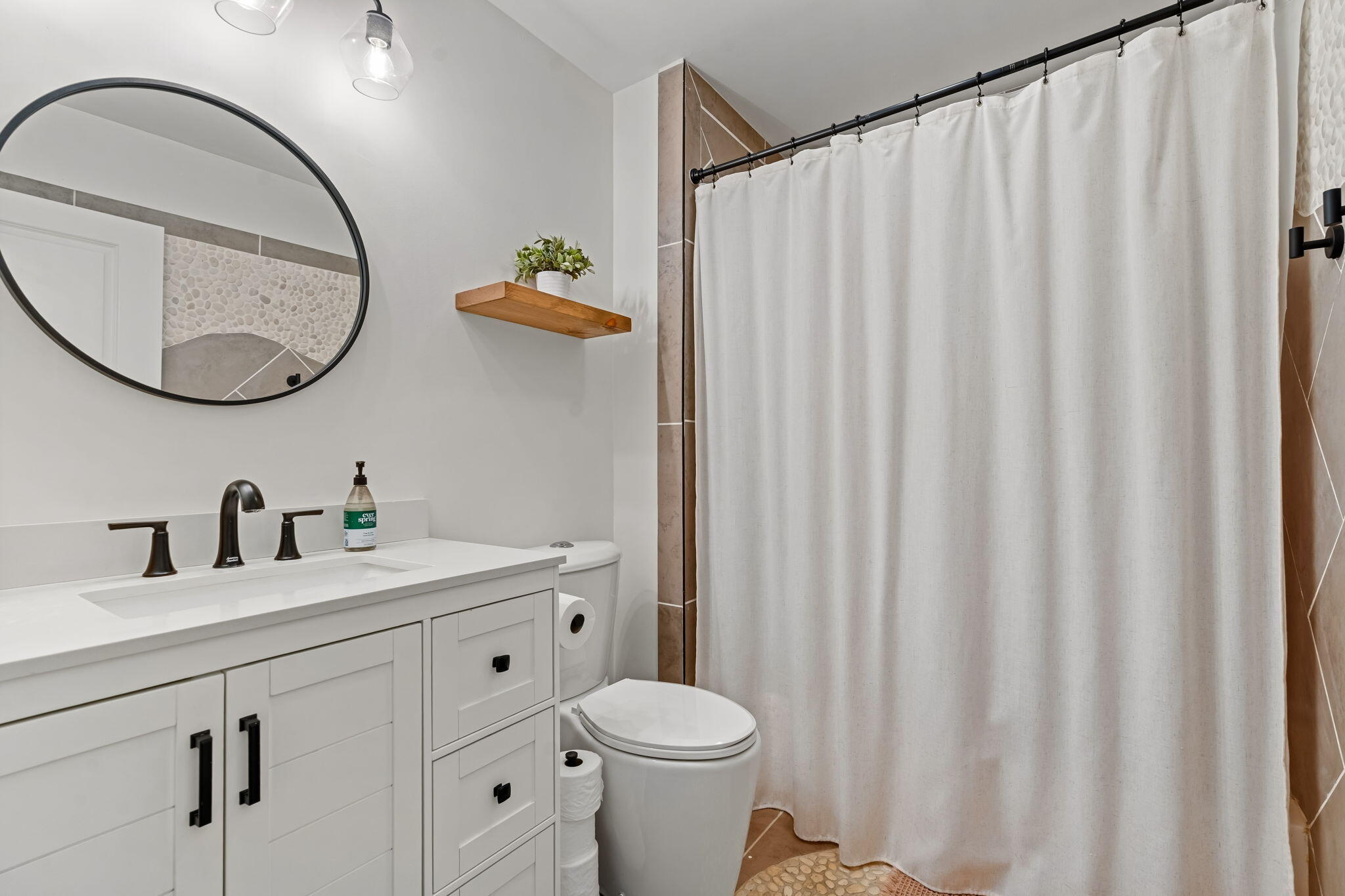 Modern bathroom with a white vanity, round mirror, and white shower curtain.
