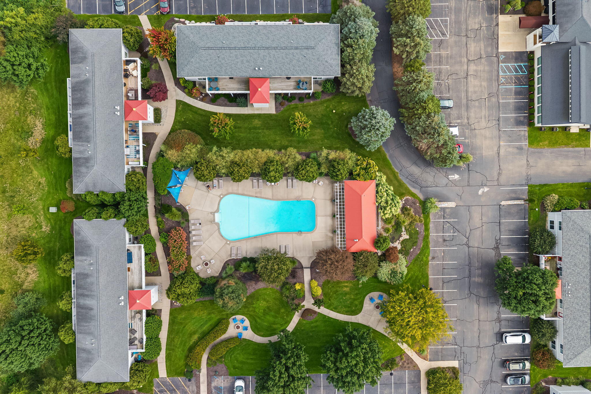Aerial view of a residential complex with a central swimming pool, landscaped paths, and parking lot.