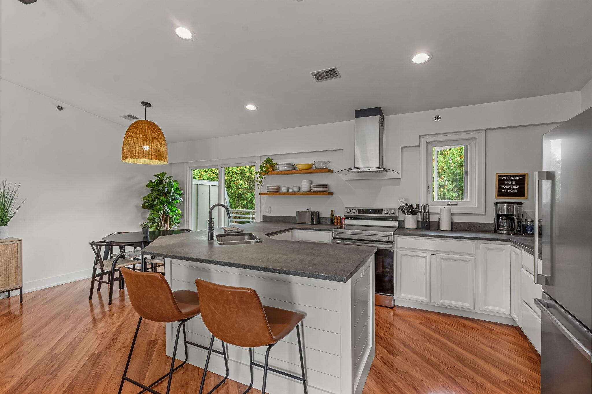 Bright kitchen with a large gray island, stainless steel appliances, open shelves, and warm hardwood floors.